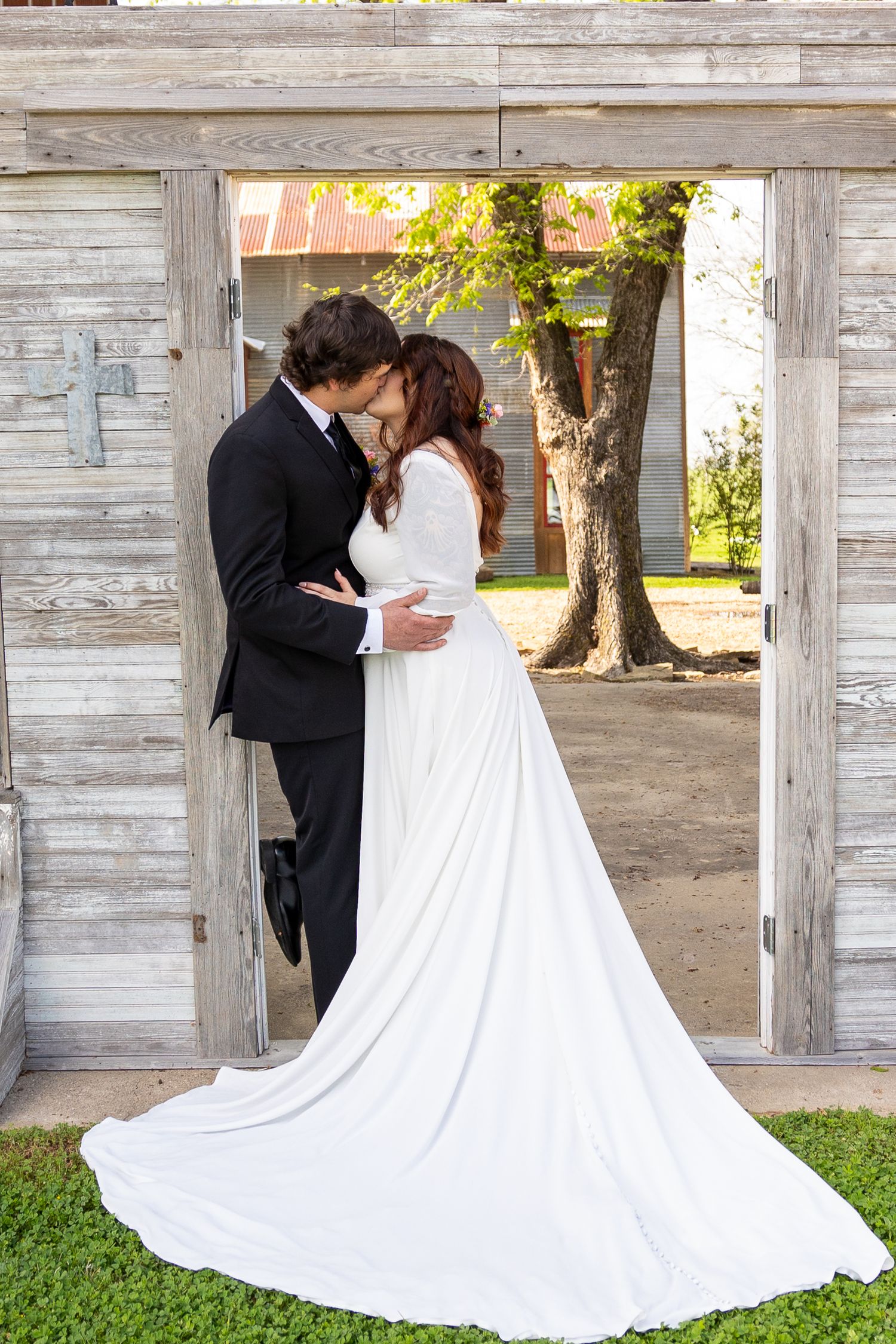Wedding couple posing against weathered white wooden wall with flowing dress train.