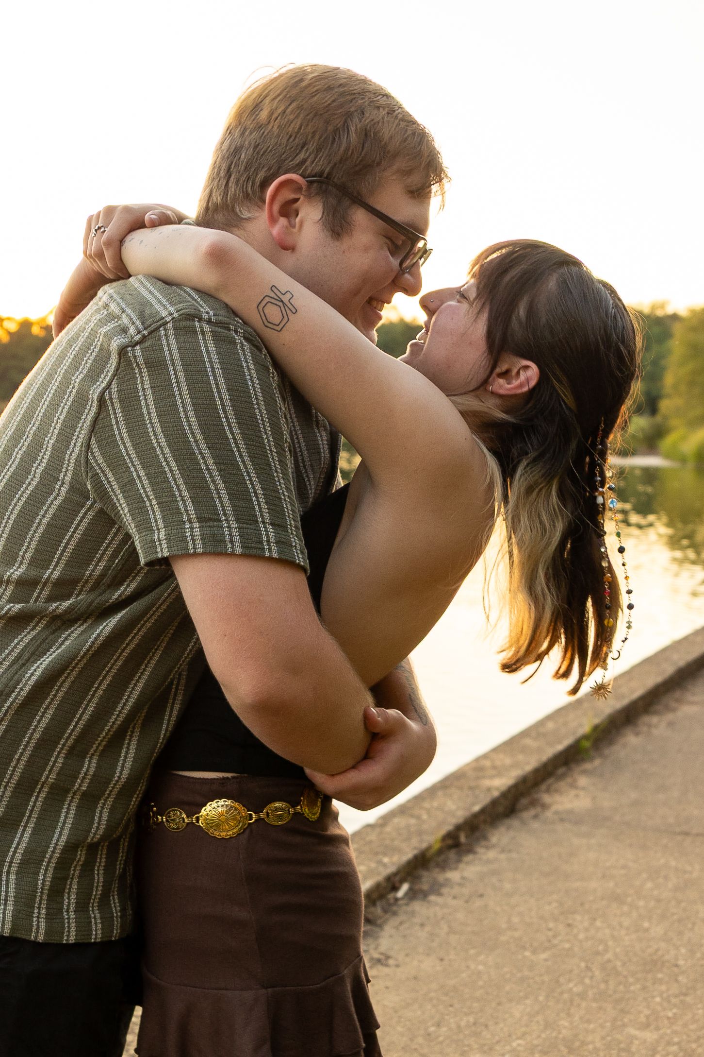 Couple sharing intimate moments by the water during sunset with dramatic lighting.