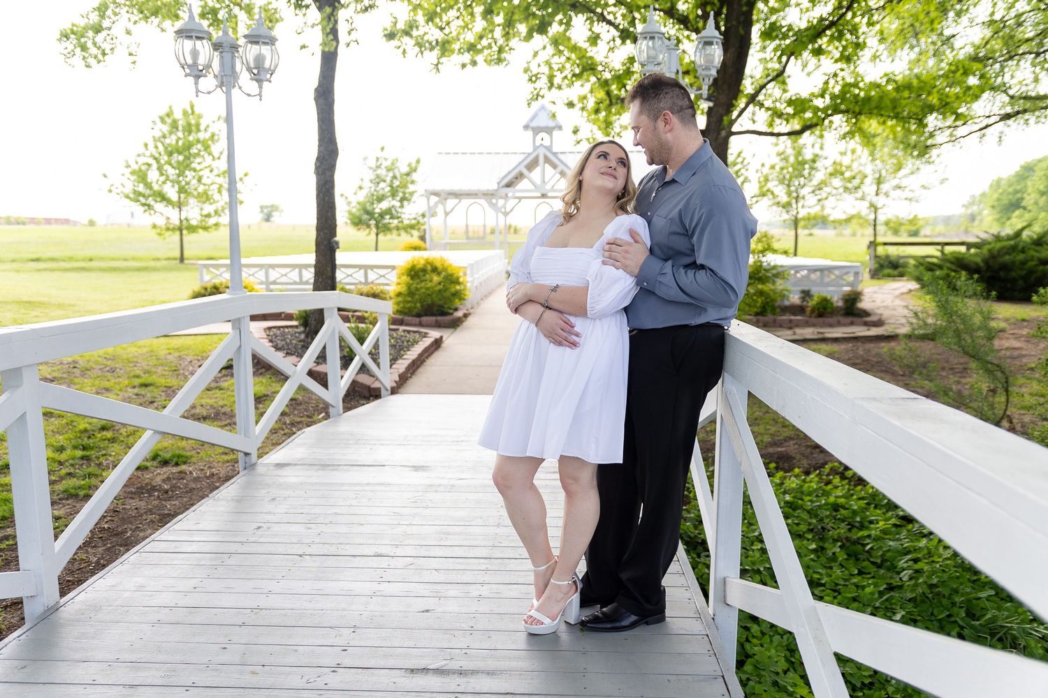 Couple sharing romantic moments on white wooden bridge in park setting.