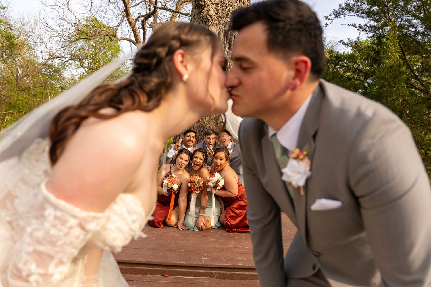 A wedding couple shares a kiss while their wedding party looks on in the background.