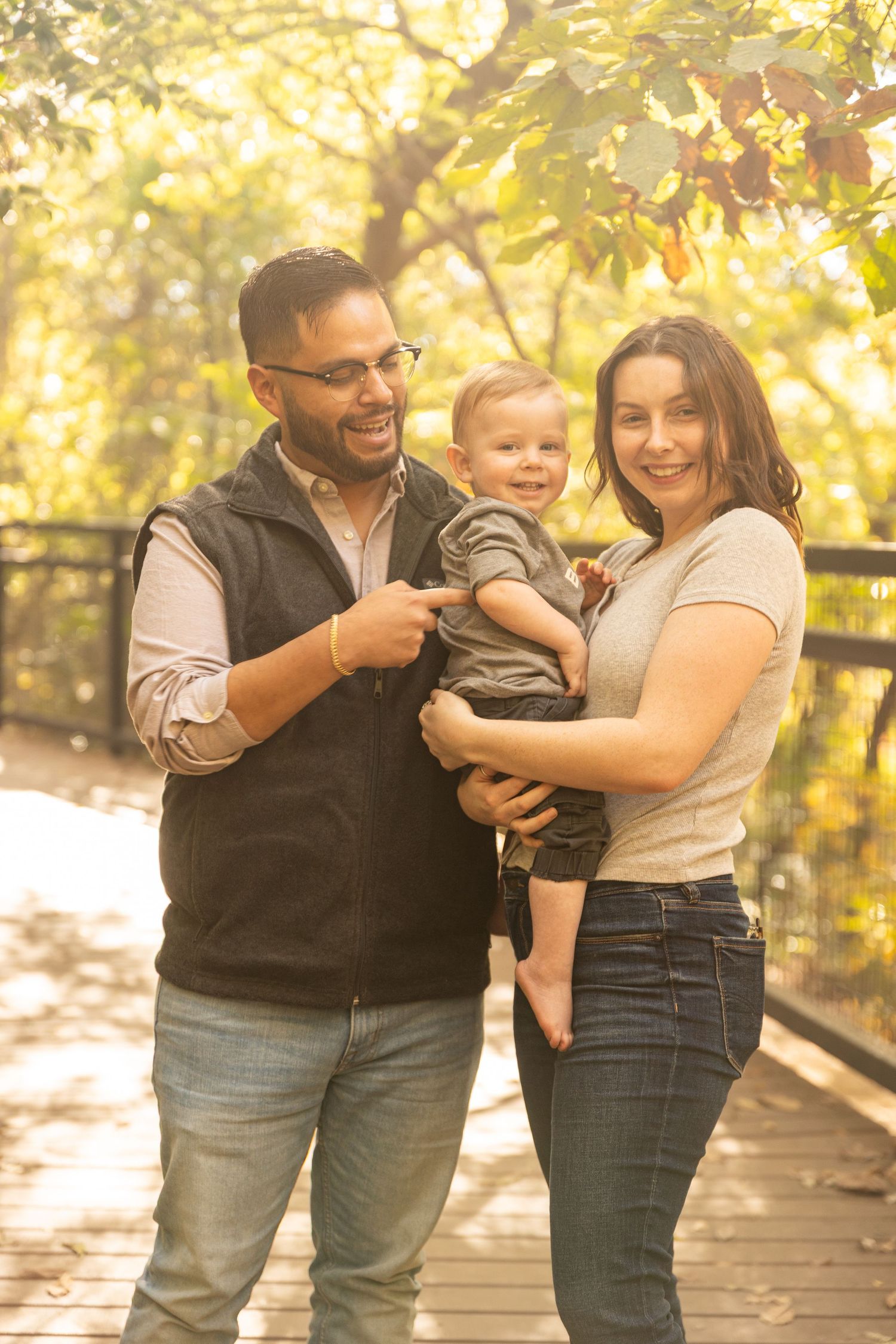 Family enjoying playful moments on a wooden boardwalk surrounded by autumn foliage during golden hour.