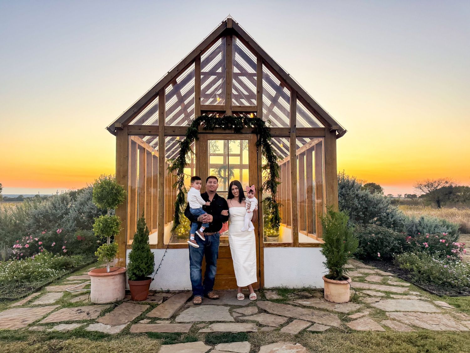 Wedding couple posing in rustic wooden greenhouse structure at sunset.