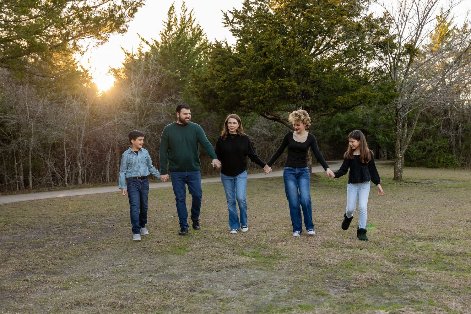 Family walking together through a grassy field at dusk with trees in background.