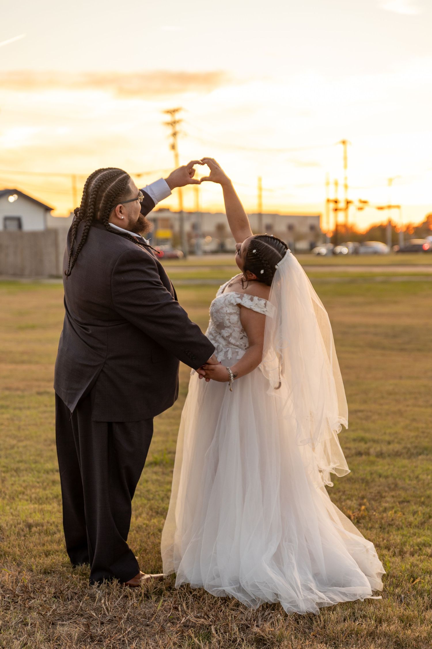 A wedding couple poses playfully in a field during sunset for their photography session.