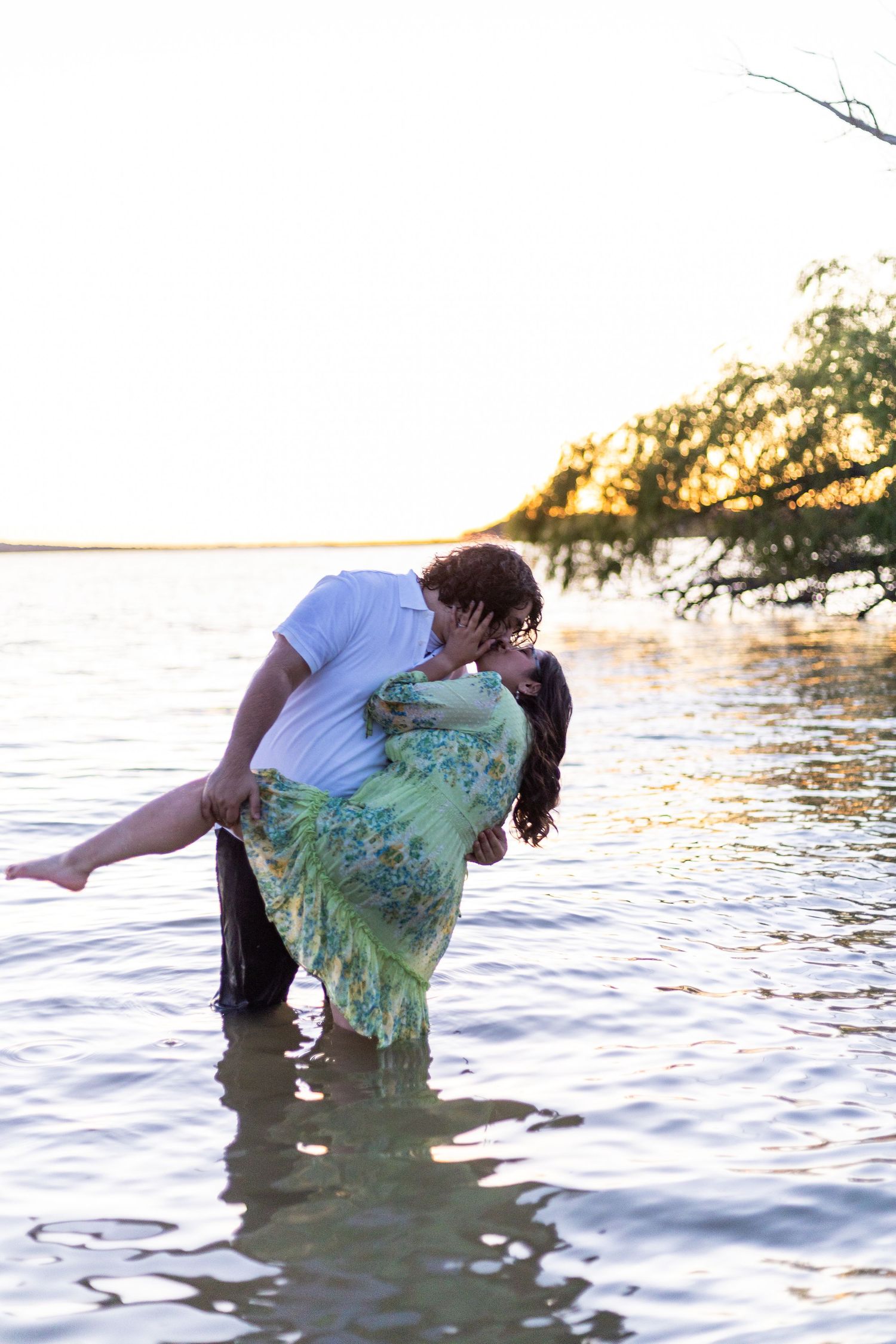 Playful couple splashes in ocean water during sunset photoshoot.