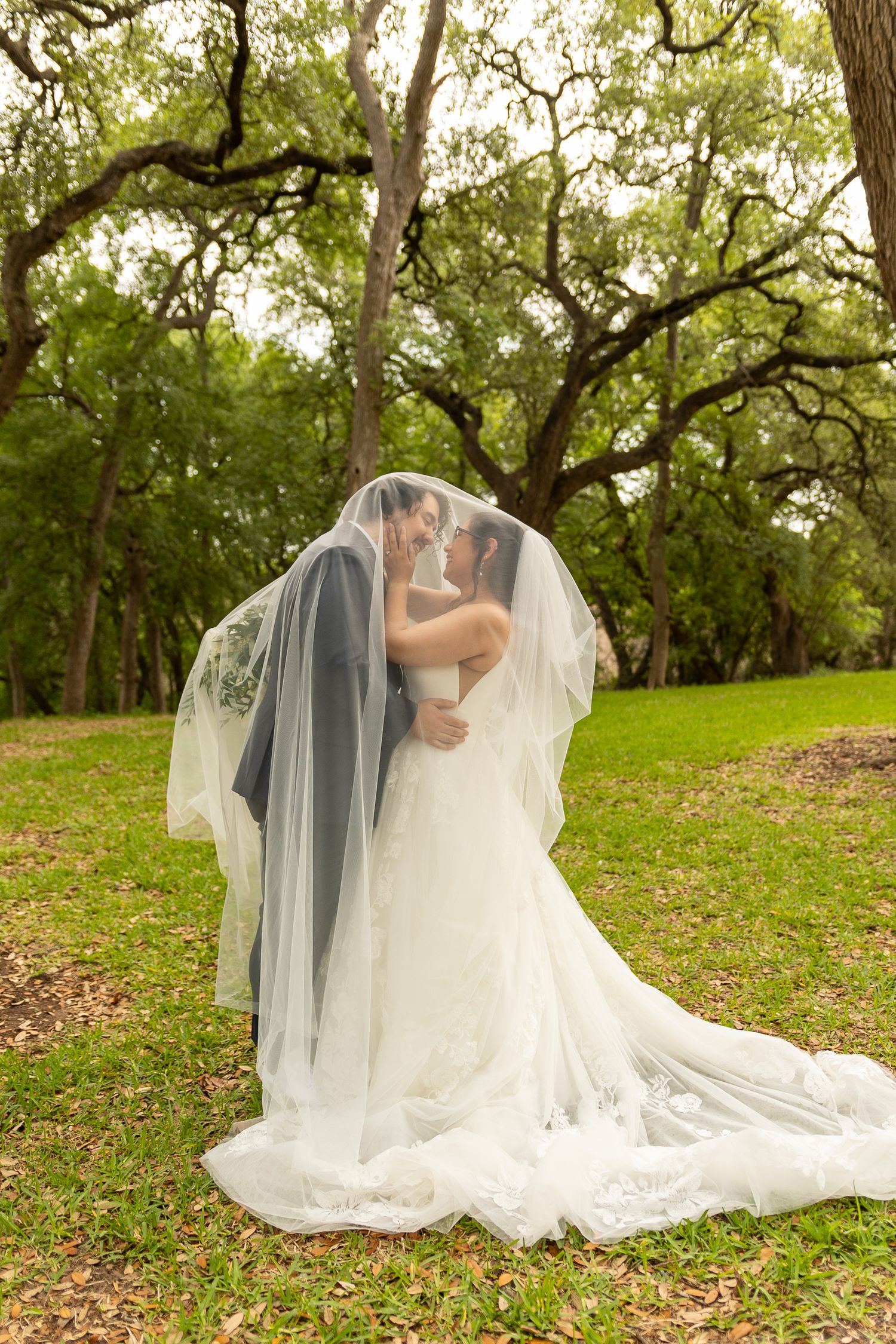 A romantic wedding couple kisses under a flowing veil in a lush garden setting.