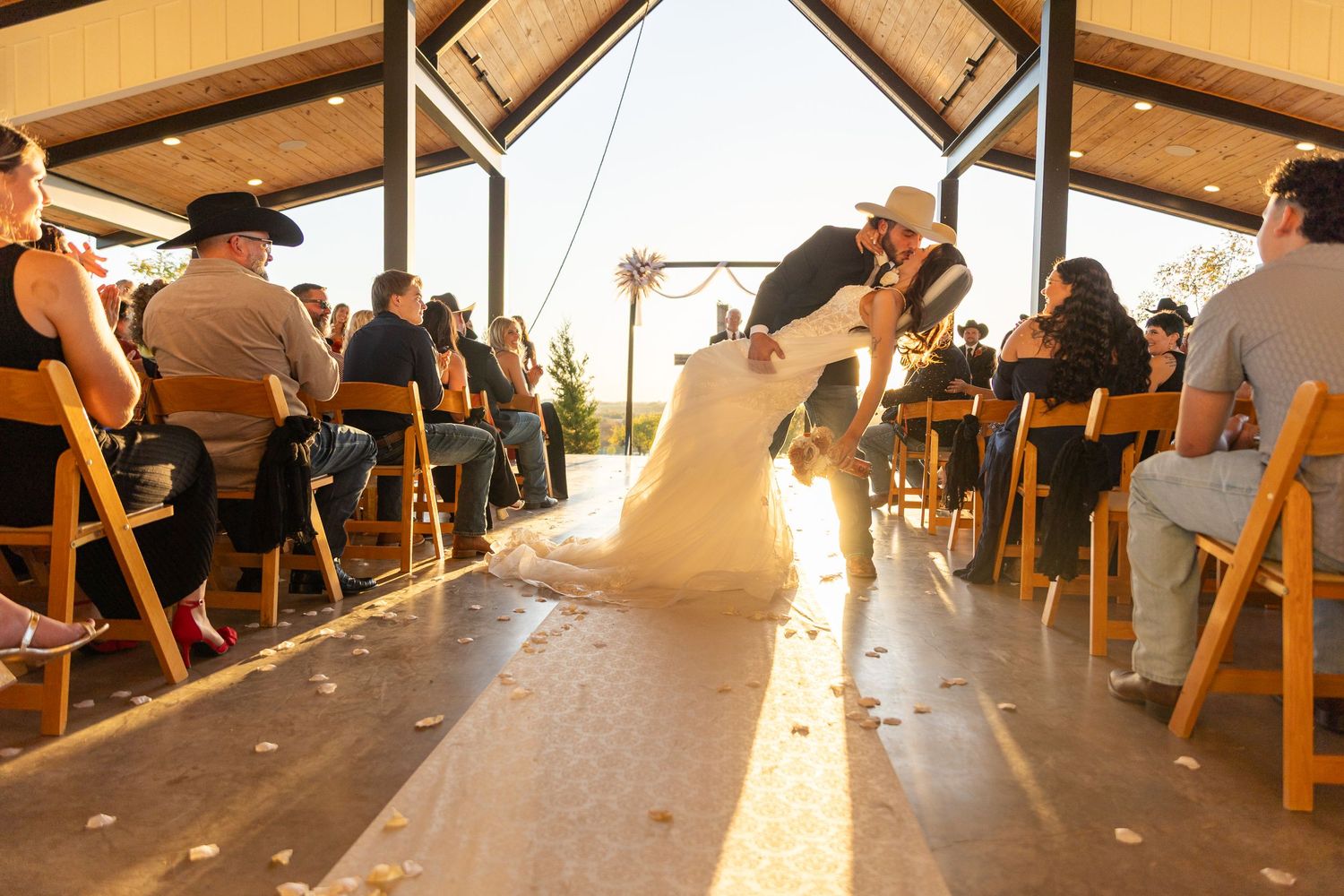 Guests seated under a large outdoor tent pavilion during a sunset wedding reception.