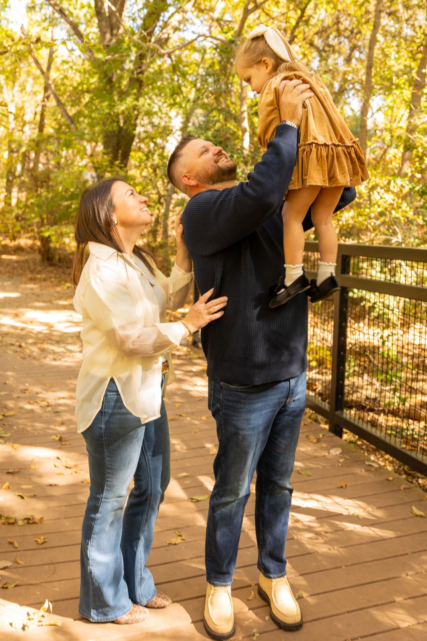 Family shares joyful moment on wooden walkway surrounded by autumn trees.