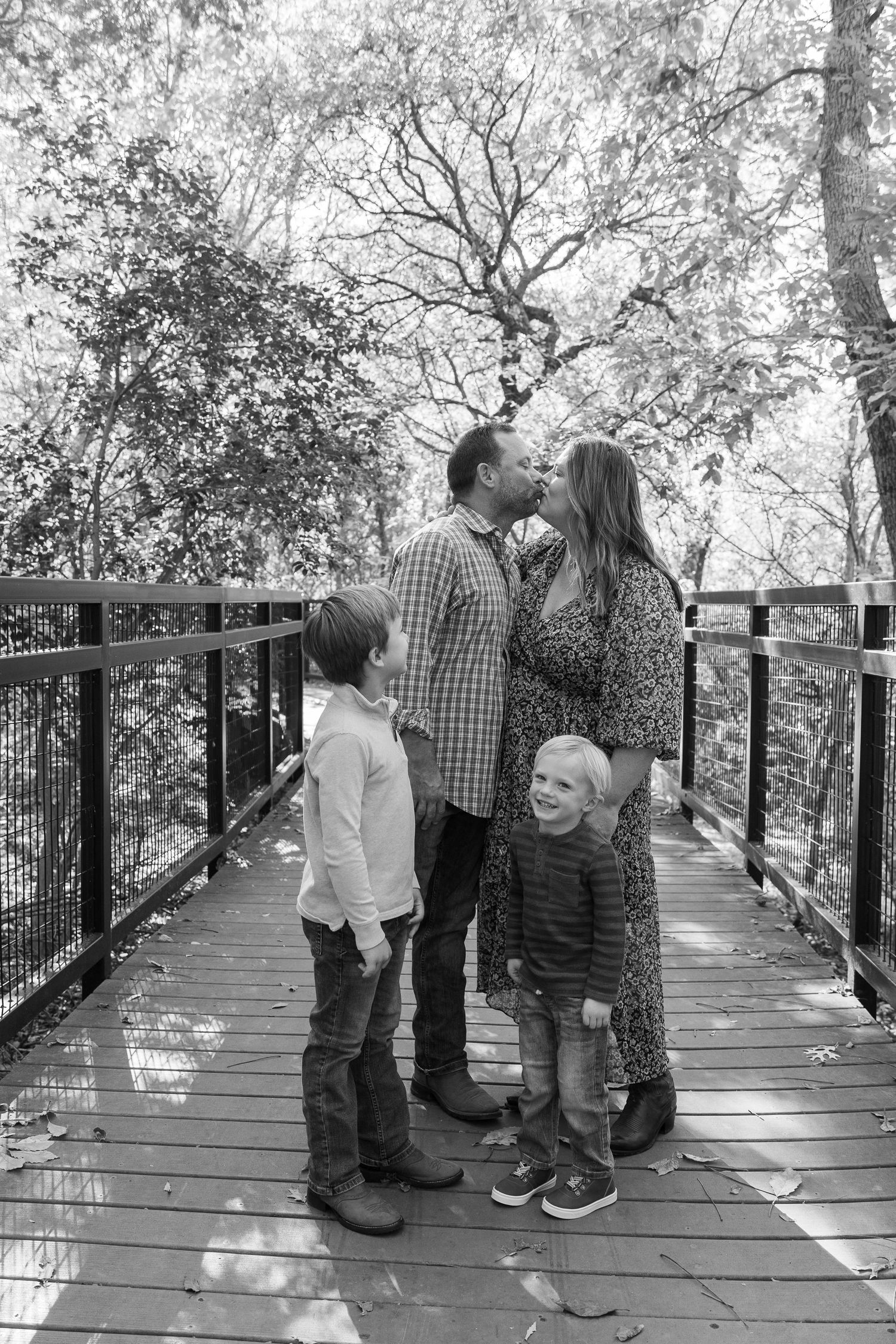 Black and white photo series of family moments on a wooden boardwalk in nature.