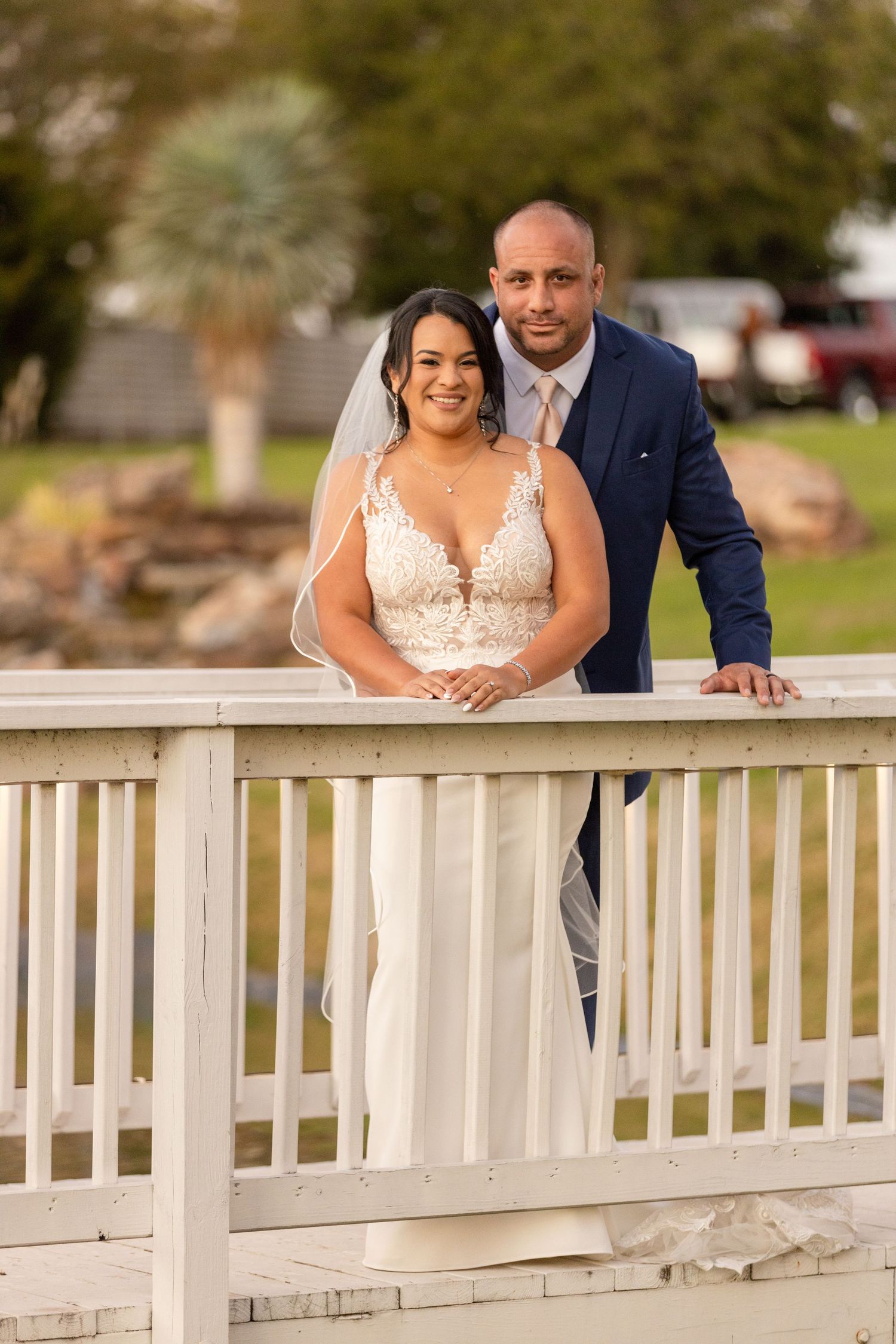 Wedding portraits of a couple posing along a white wooden railing outdoors.
