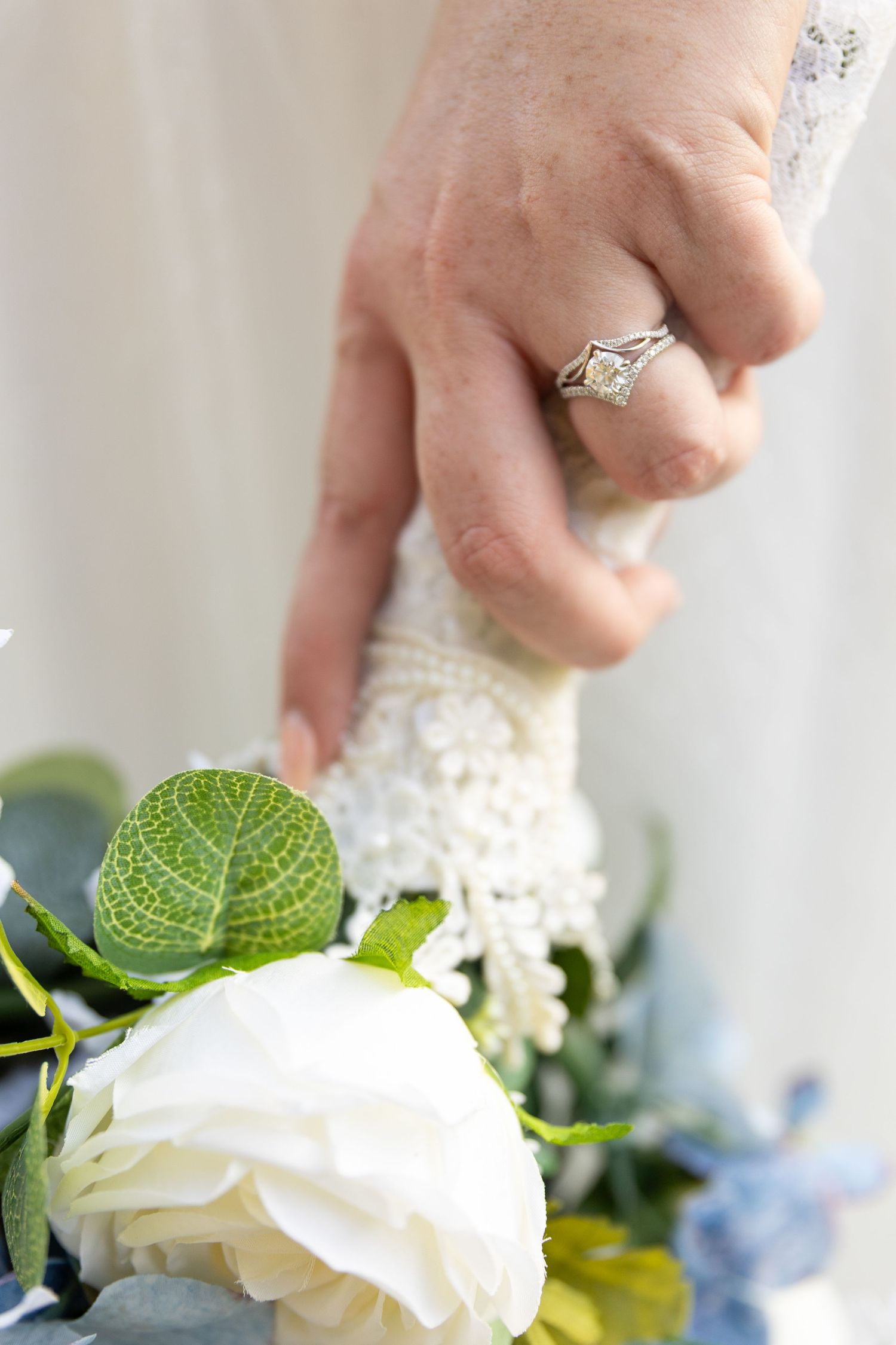 White roses and greenery in a wedding bouquet with engagement ring detail.