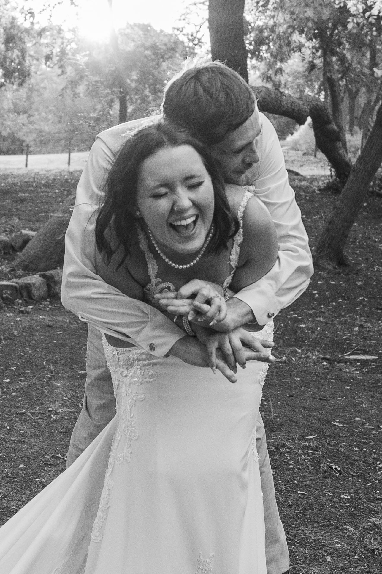 Candid black and white wedding photos showing playful moment between couple embracing outdoors.