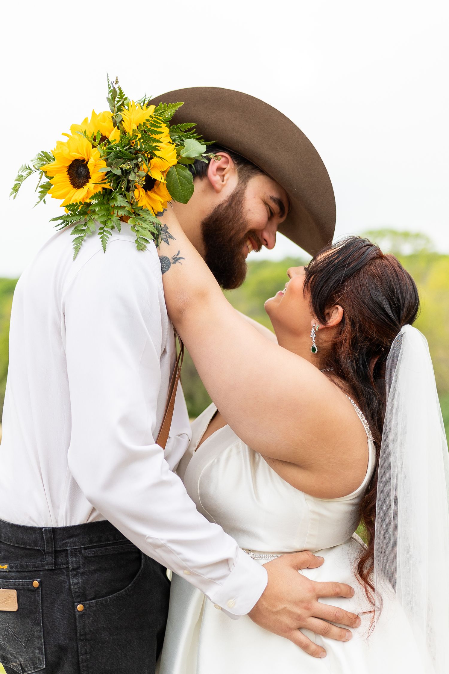 A romantic couple embraces while wearing western attire with sunflowers decorating the groom's hat.