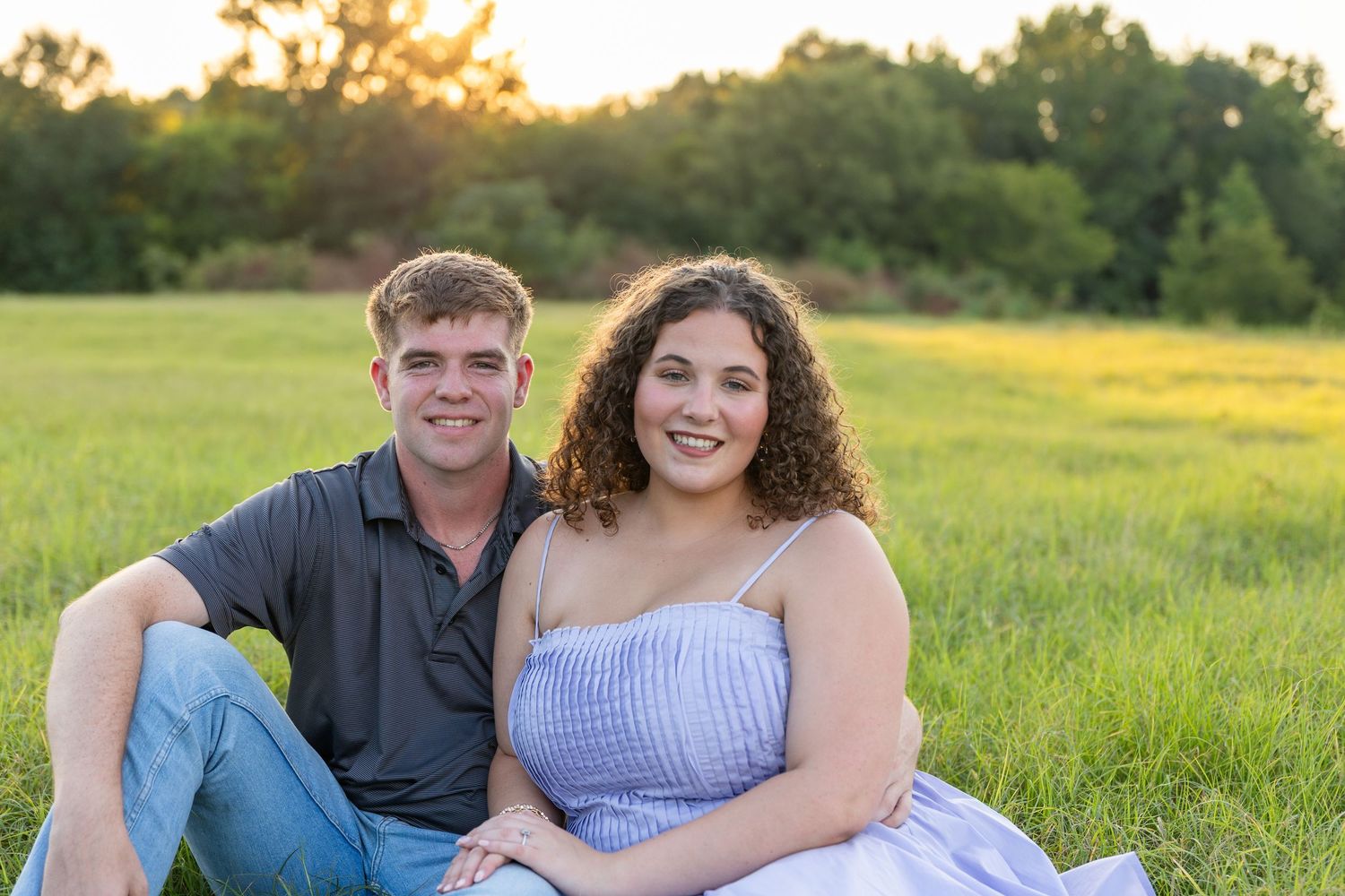 Couple in casual attire sharing tender moments in a sunny meadow.