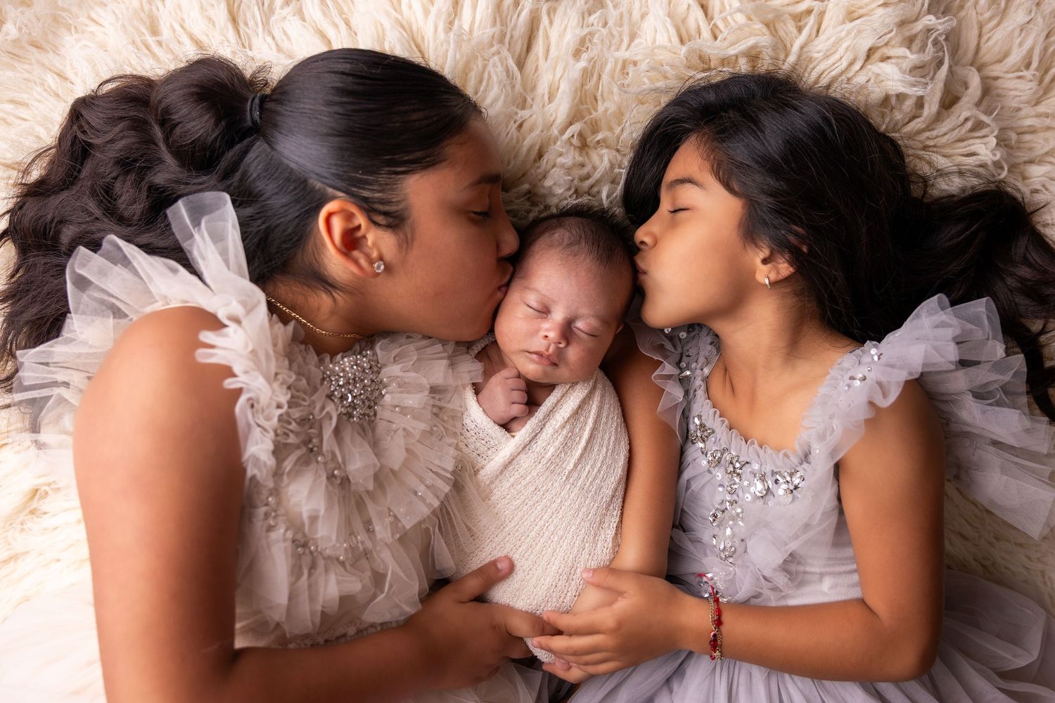 Family lying together on fluffy cream-colored blanket in intimate portrait series.