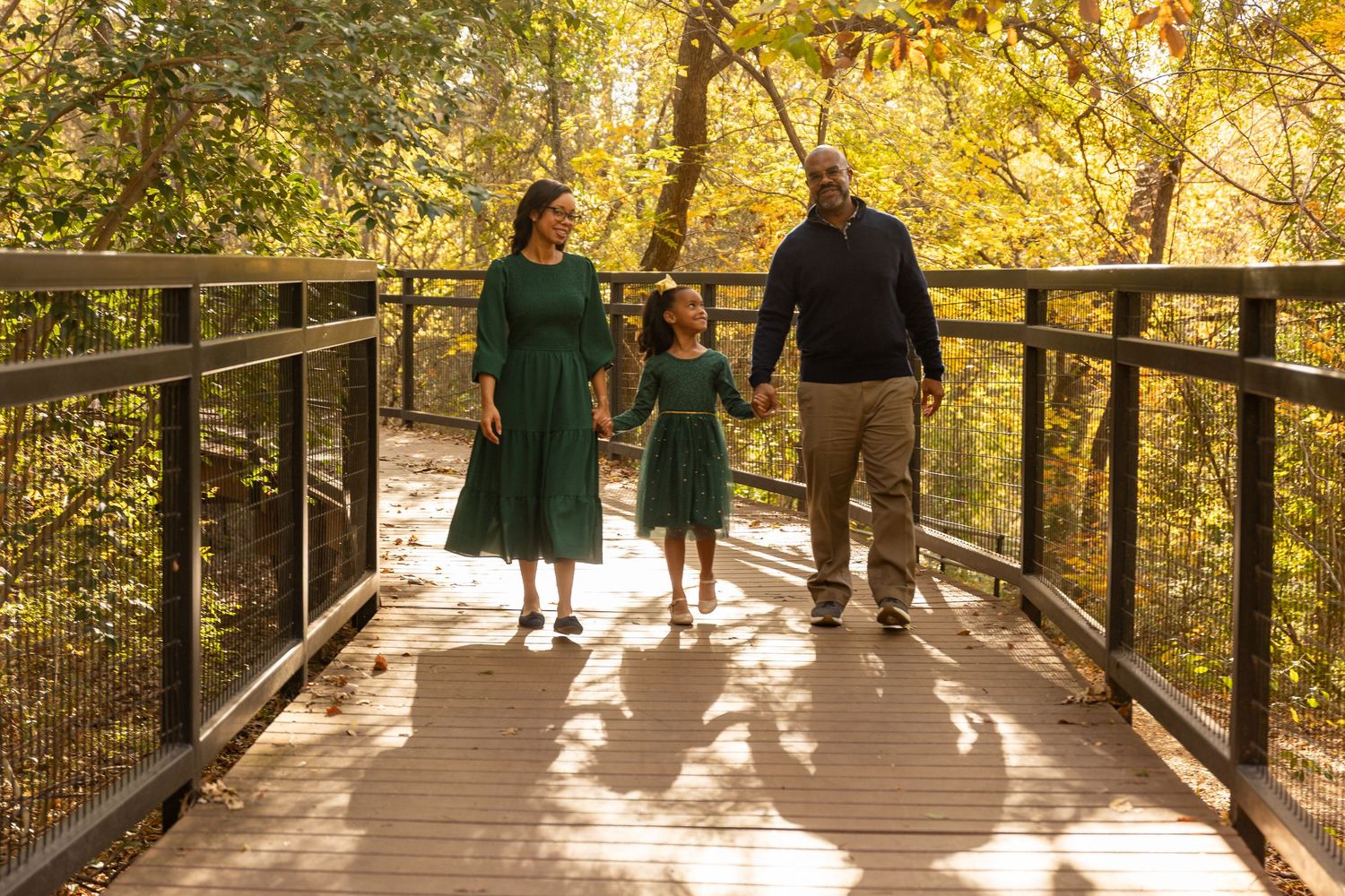Family walking together on elevated wooden boardwalk surrounded by autumn trees.