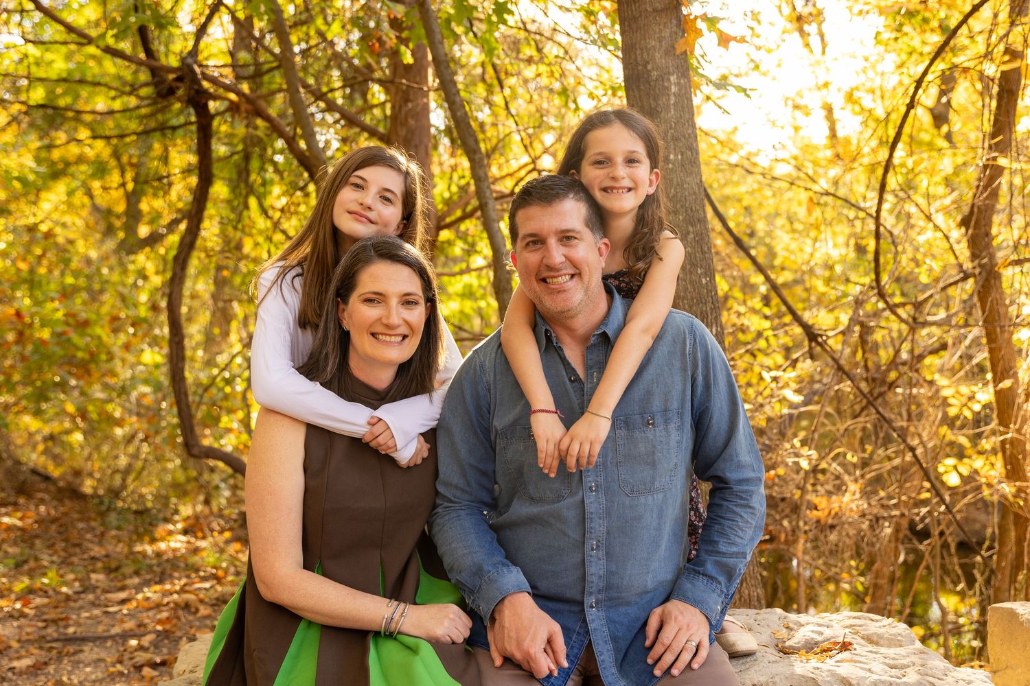 Family portrait outdoors with golden autumn foliage in background.
