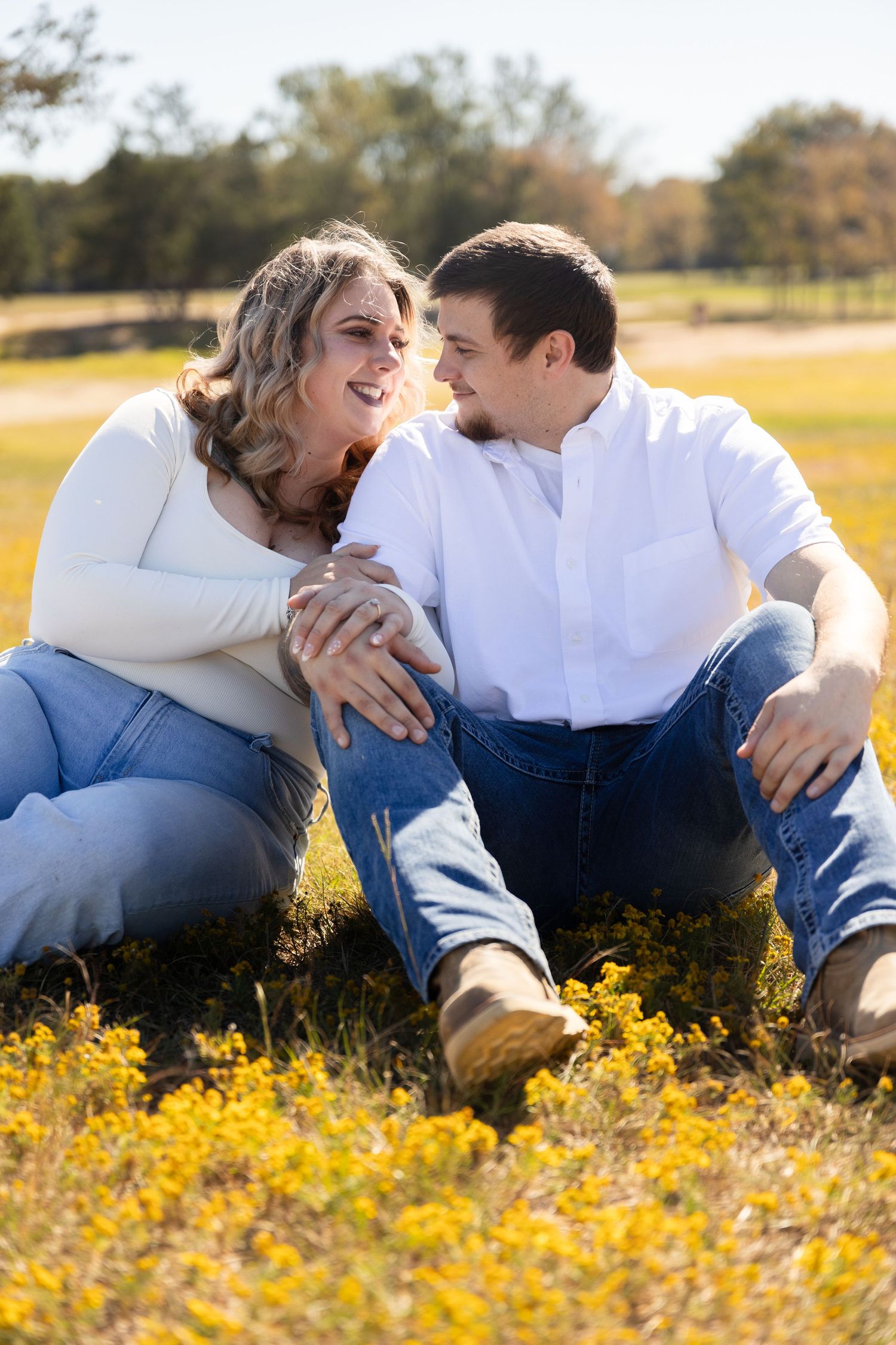 Couple sitting together in a field of yellow wildflowers during golden hour.
