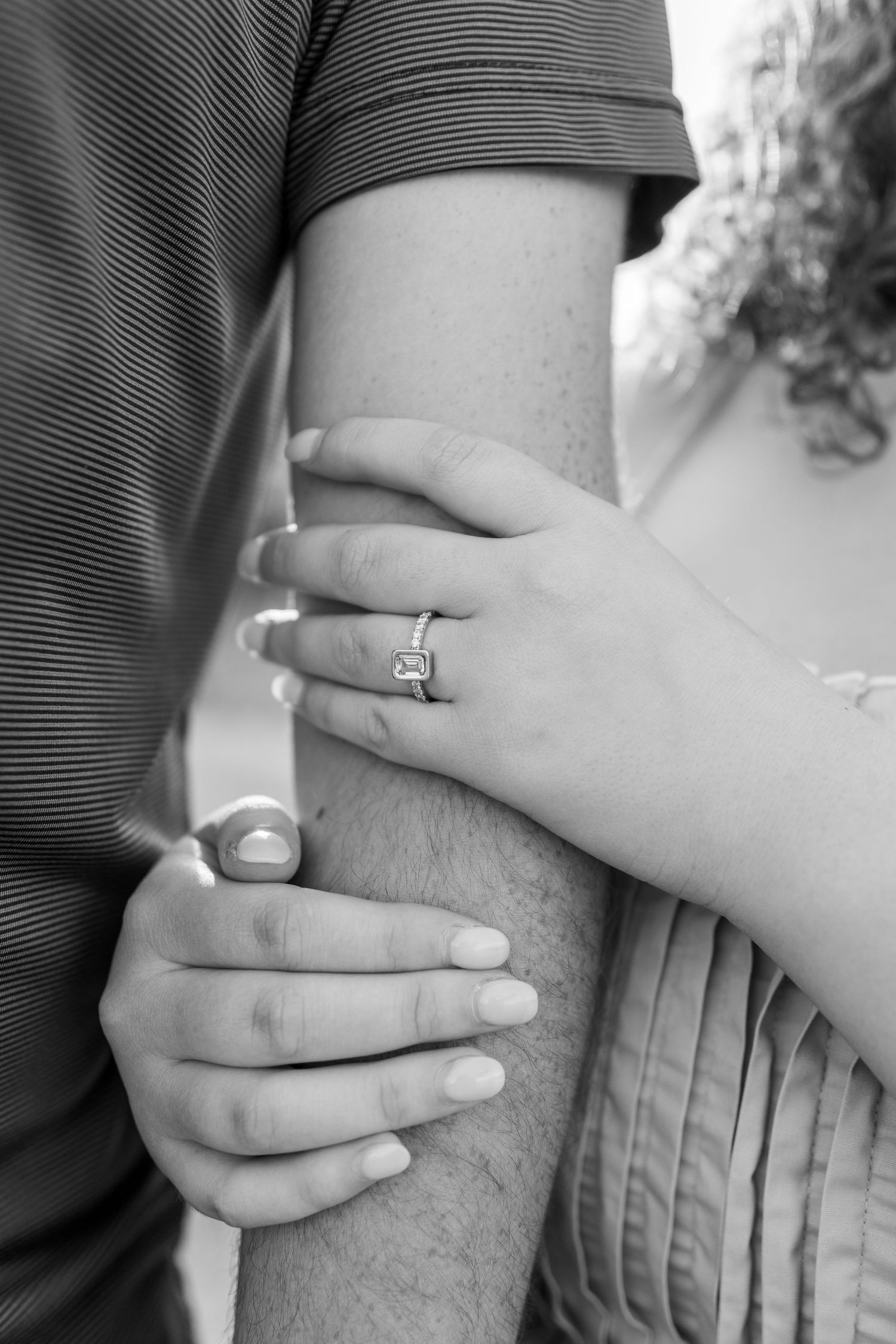 Close-up of hands showing an engagement ring and gentle embrace.