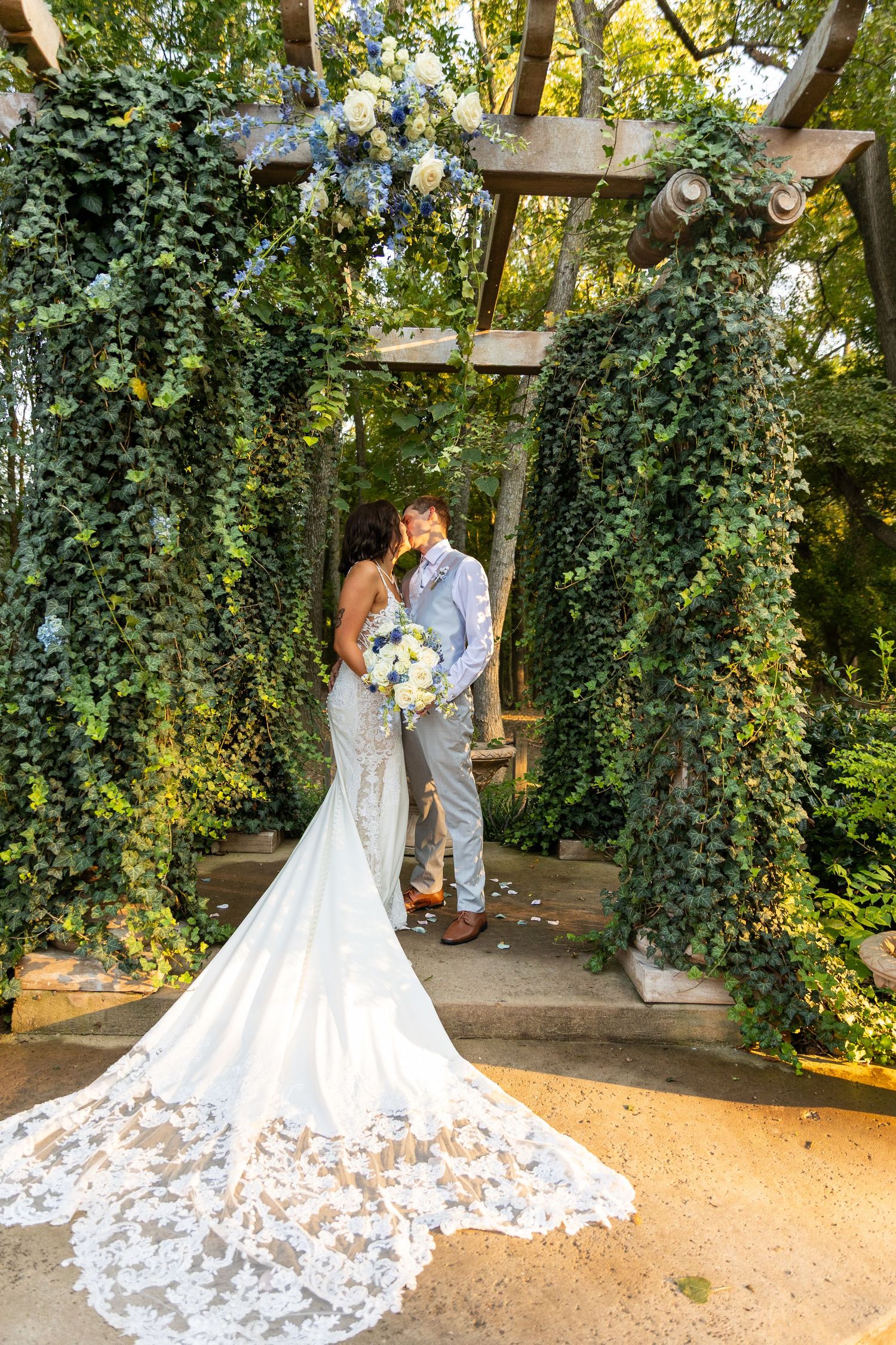 Beautiful wedding dress train with intricate lace details spread out under an ivy-covered pergola.