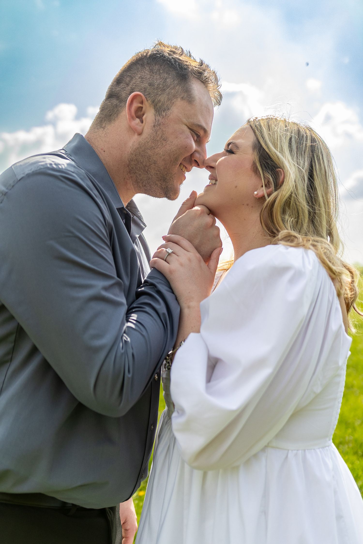 A tender moment between a couple in a sunny meadow with white clothing.