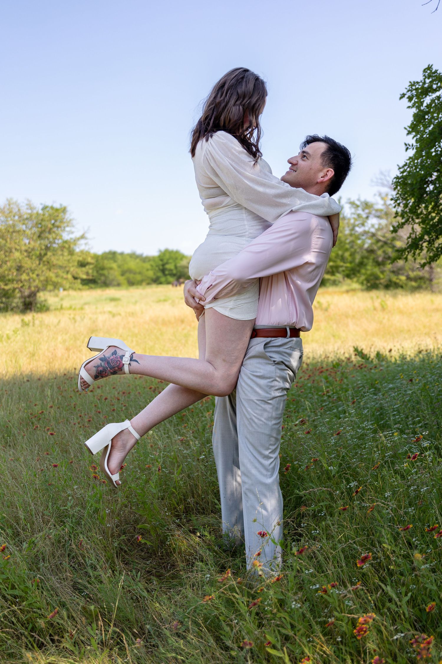Romantic couple in light colored clothing embracing and dancing in wildflower field.