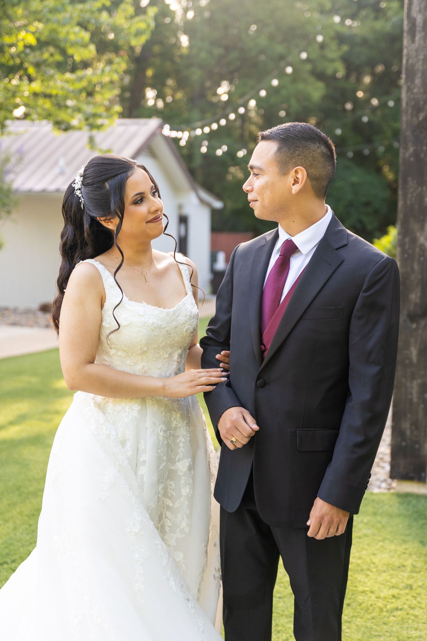 Couple shares candid laughs during outdoor wedding portraits on sunny lawn.