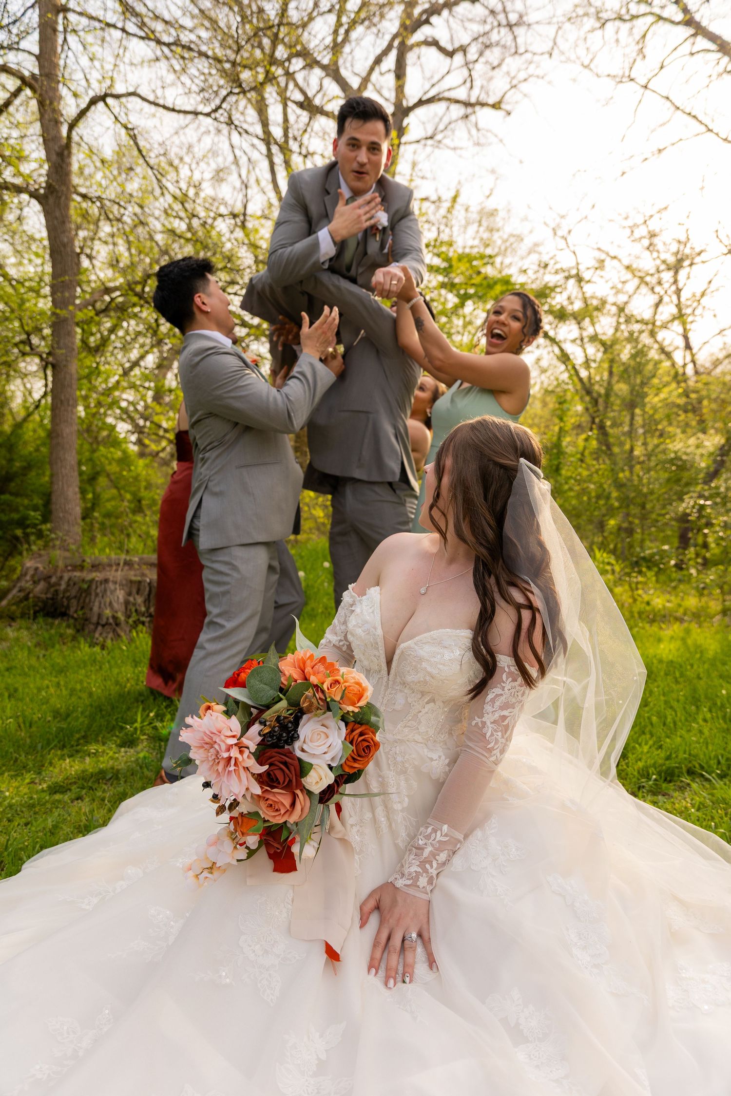 Groomsmen lift the groom while the bride looks on with her bouquet during wedding photos.