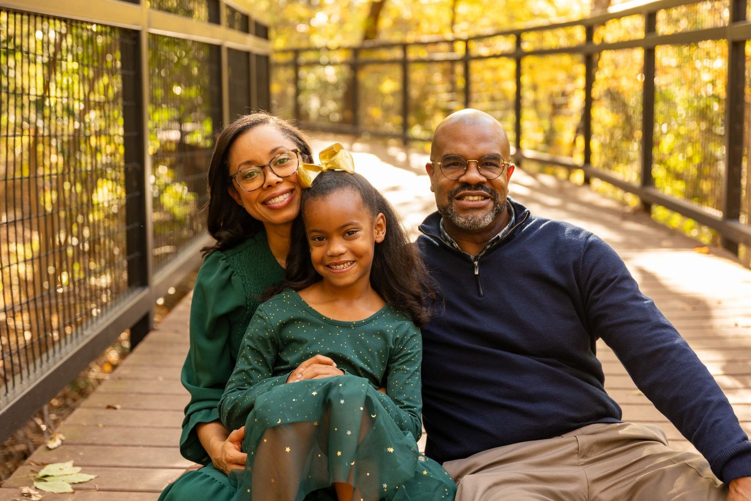 A family sits together on a wooden bridge surrounded by golden autumn foliage.