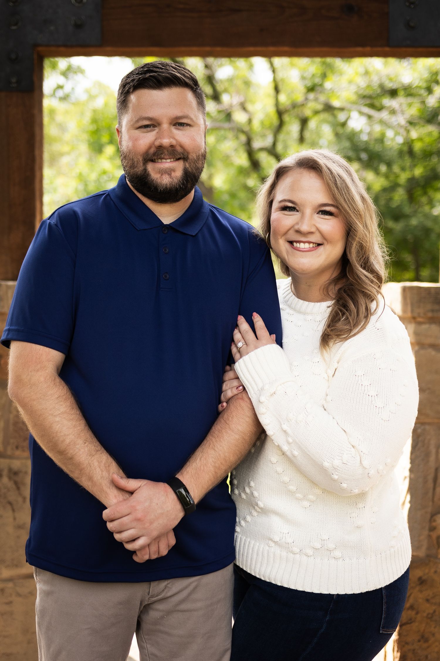 Couple in navy and white outfits posing together against rustic stone backdrop.