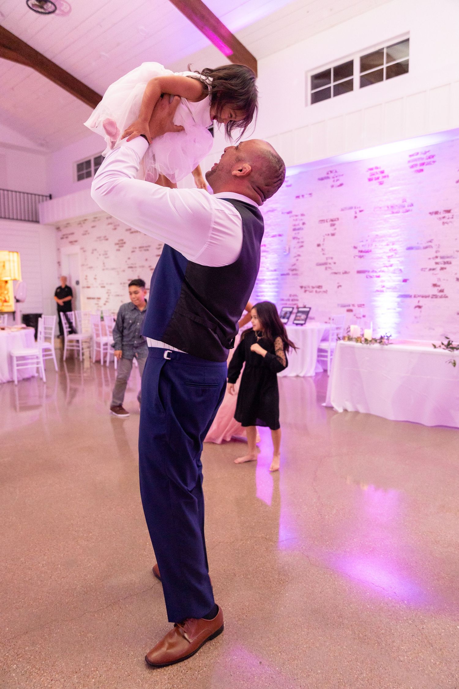 Couple dancing together in an elegant ballroom with pink lighting and white walls.