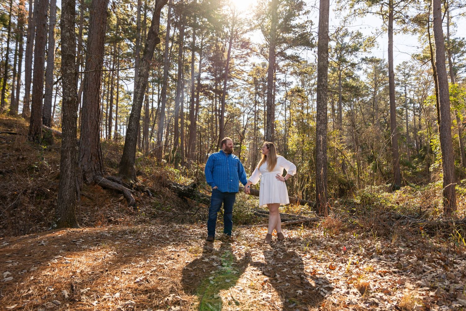Couple walking through a sunlit forest path during autumn with golden light filtering through trees.
