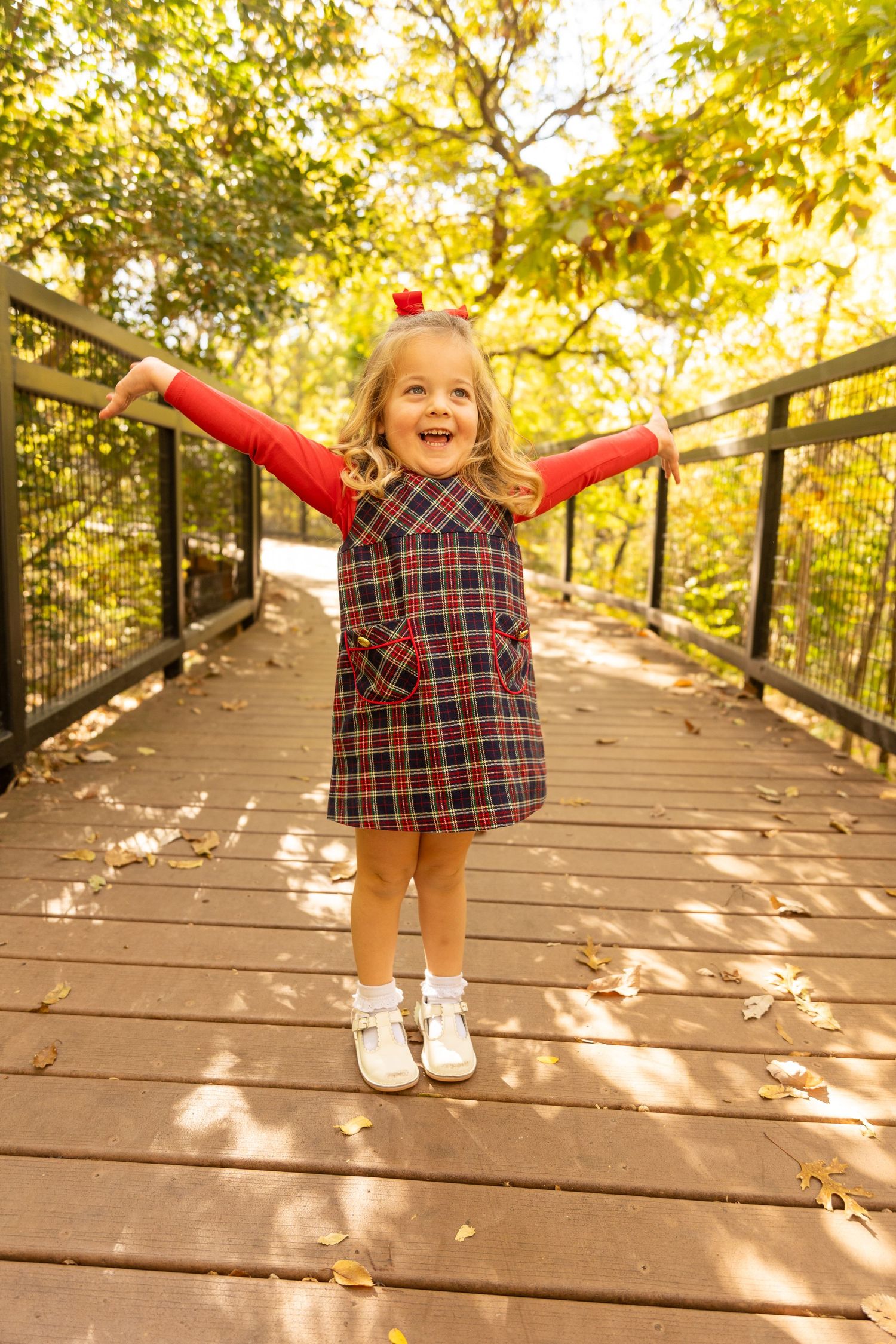 Child jumping with joy on wooden boardwalk surrounded by autumn foliage and golden light.