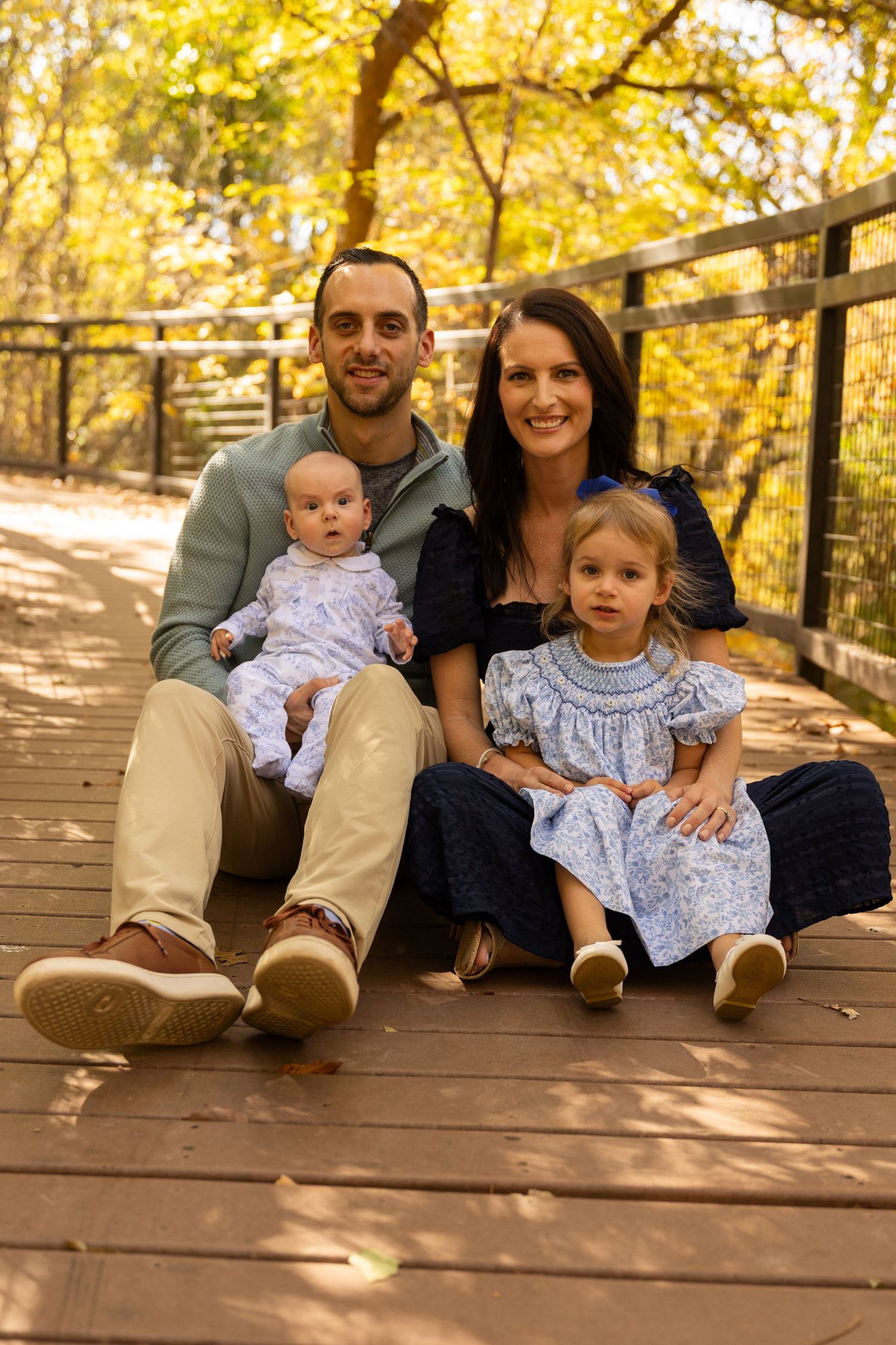 Family relaxes together on wooden deck during autumn photo session with golden lighting.