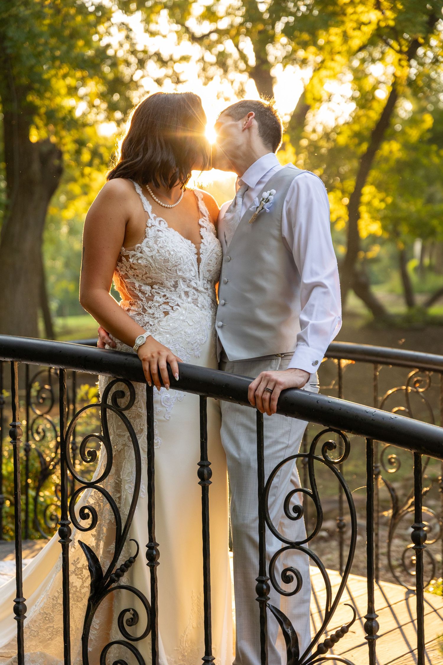 Romantic sunset portraits of newlyweds against ornate iron railing with golden light filtering through trees.