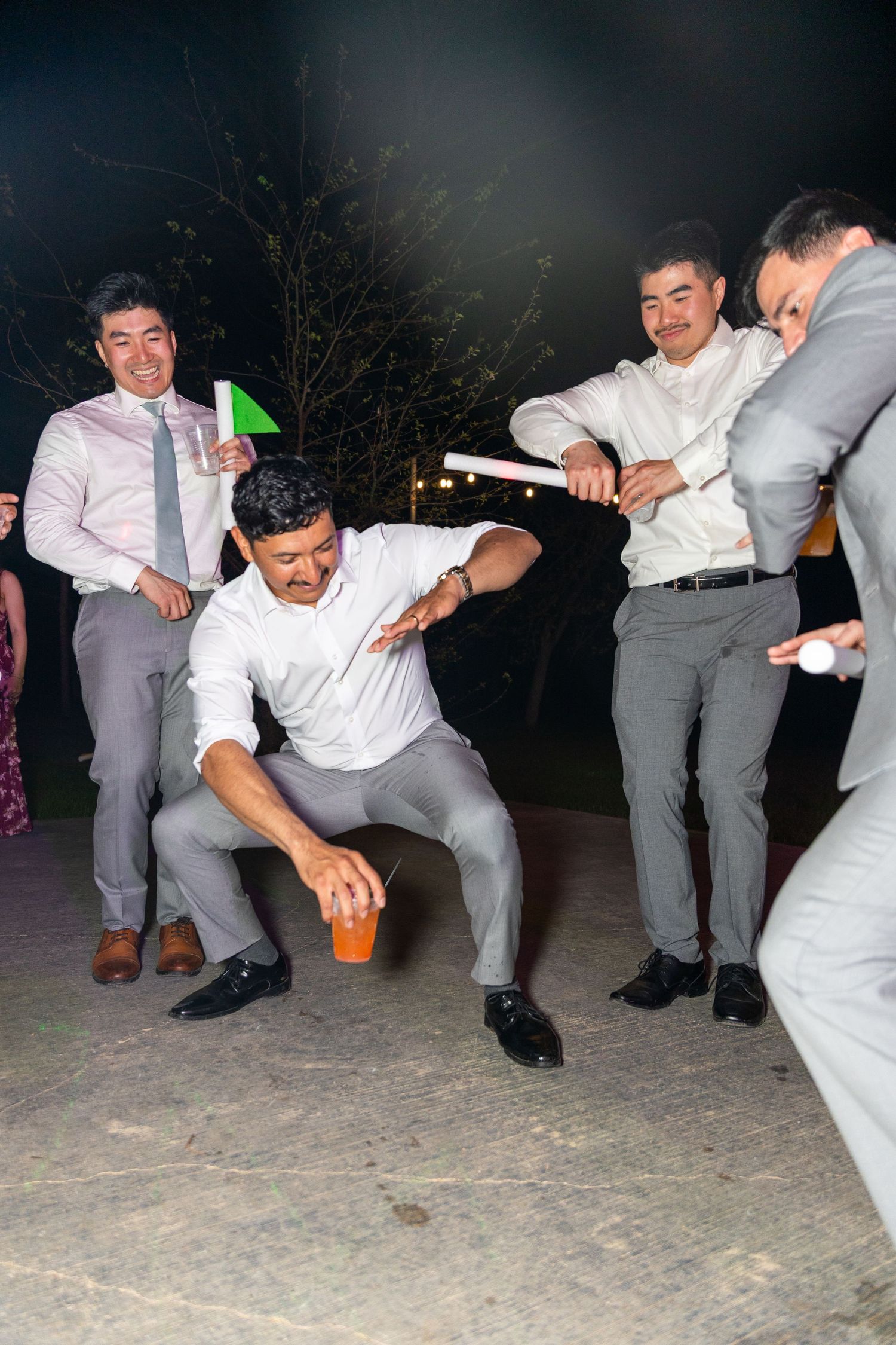 Wedding party members in grey suits performing synchronized dance moves at night reception.