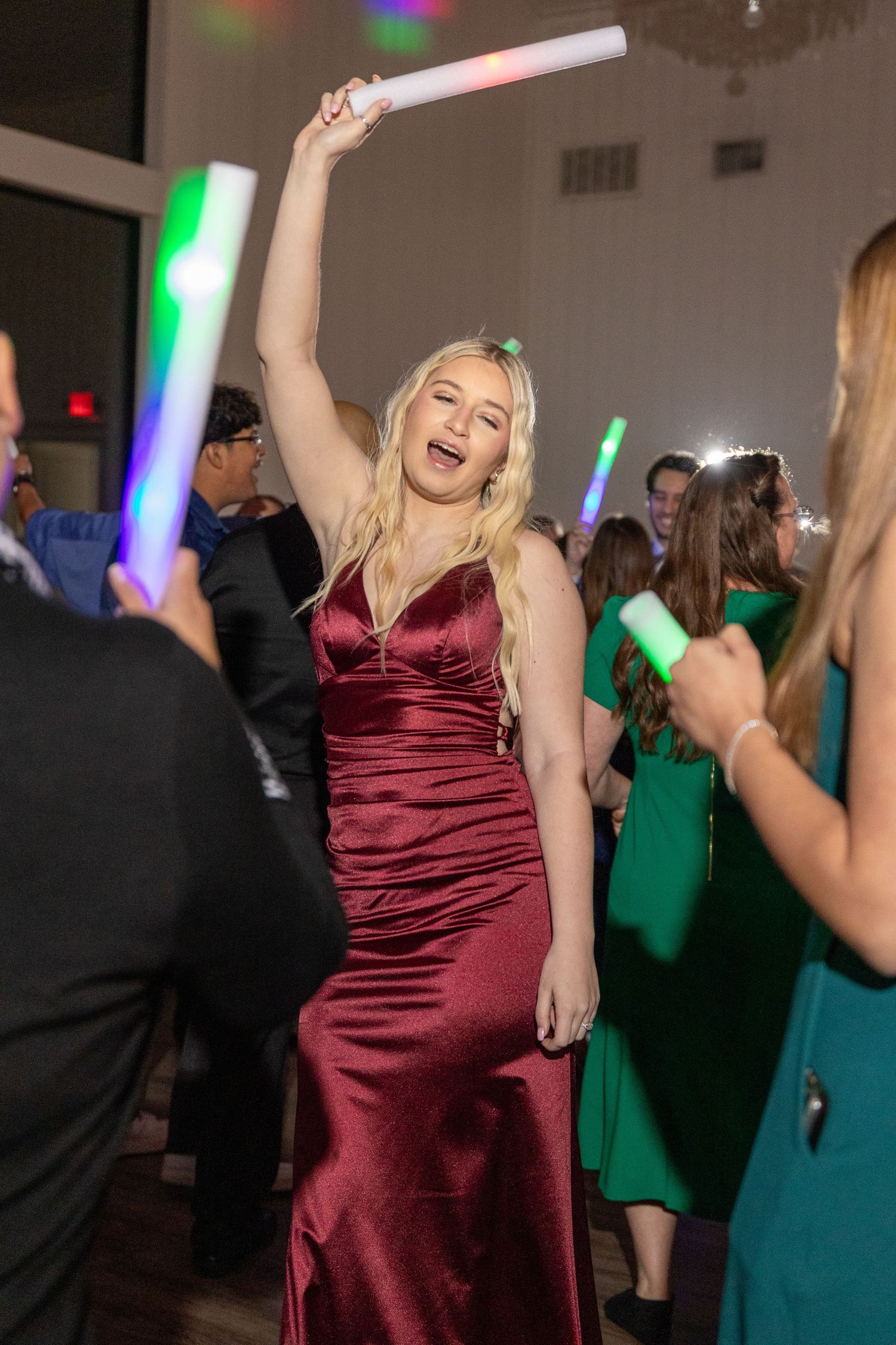 Guests dancing with glow sticks at wedding reception under colorful lights.