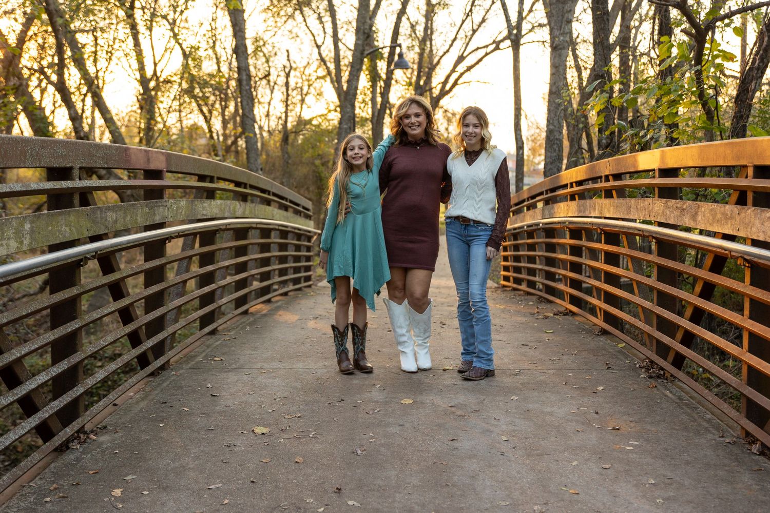 People walking across a wooden bridge surrounded by autumn trees at sunset.