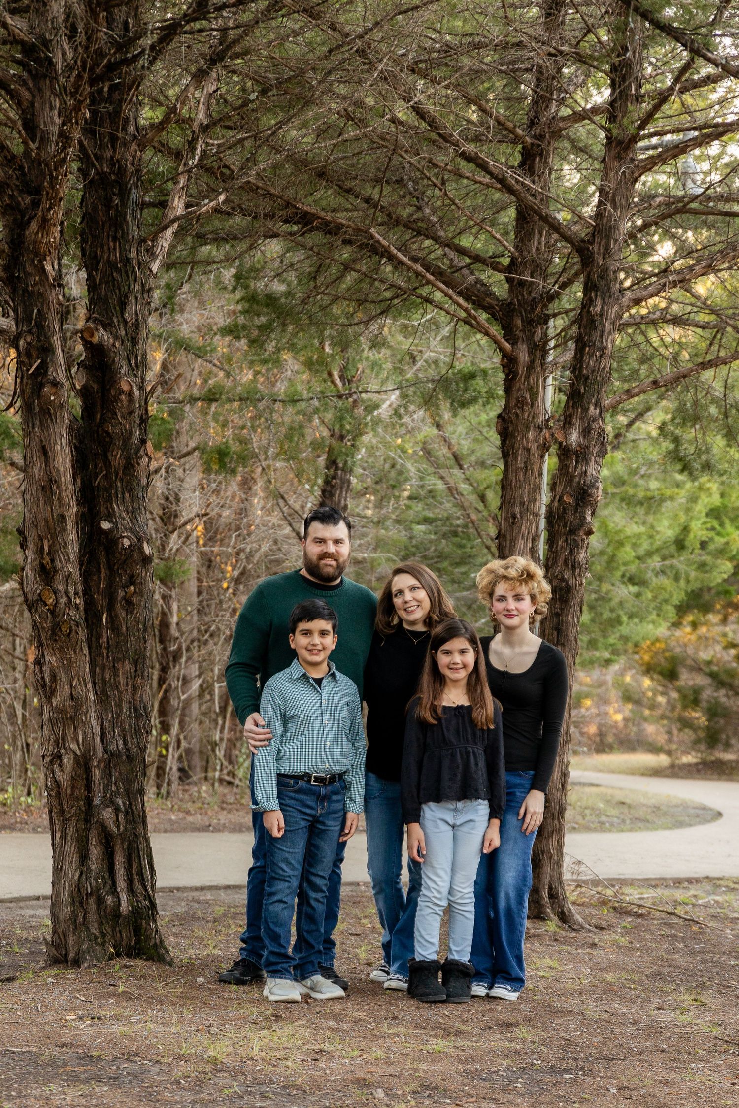 Family group photo under tall pine trees in a wooded outdoor setting.