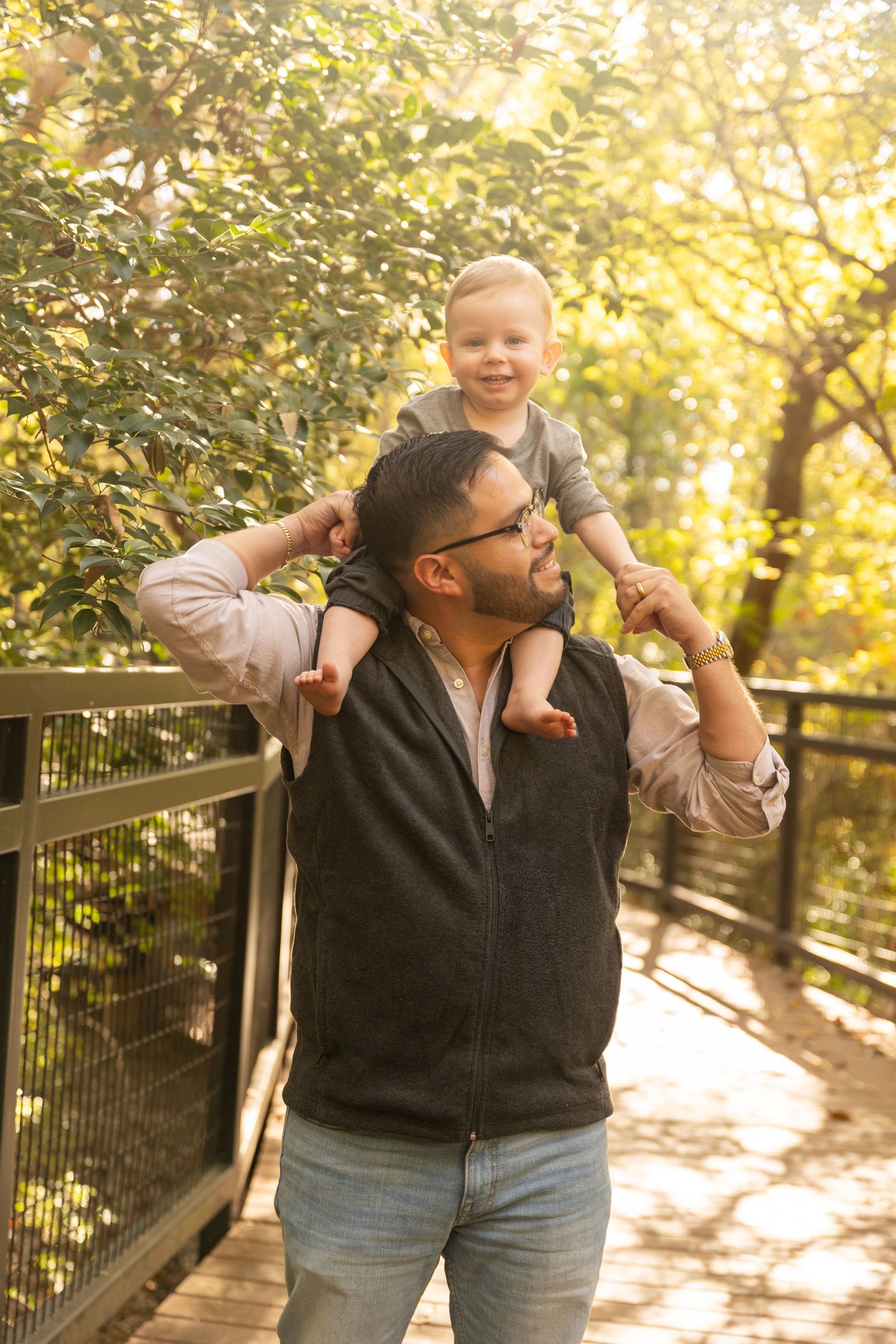 Joyful family moment captured on wooden walkway with golden sunlight streaming through trees.