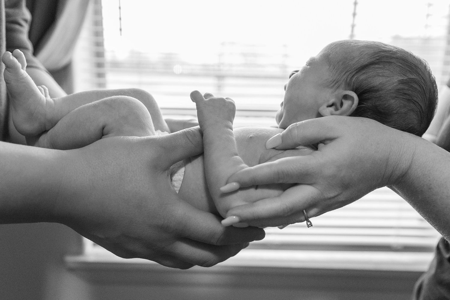 Black and white image of hands gently holding a newborn baby.