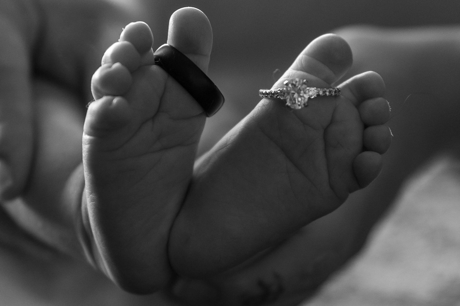 A black and white close-up photograph of tiny baby feet with a ring placed between them.