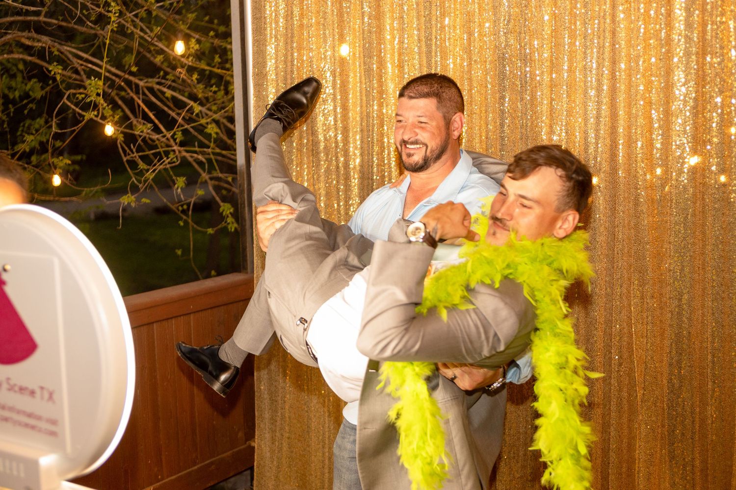 Wedding guests having fun in a photo booth with props and a gold sequin backdrop.