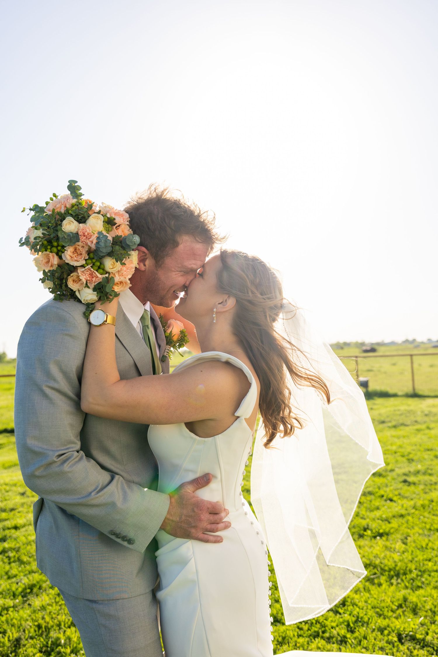 Romantic wedding portrait in sunlit field with bride's veil catching golden light.