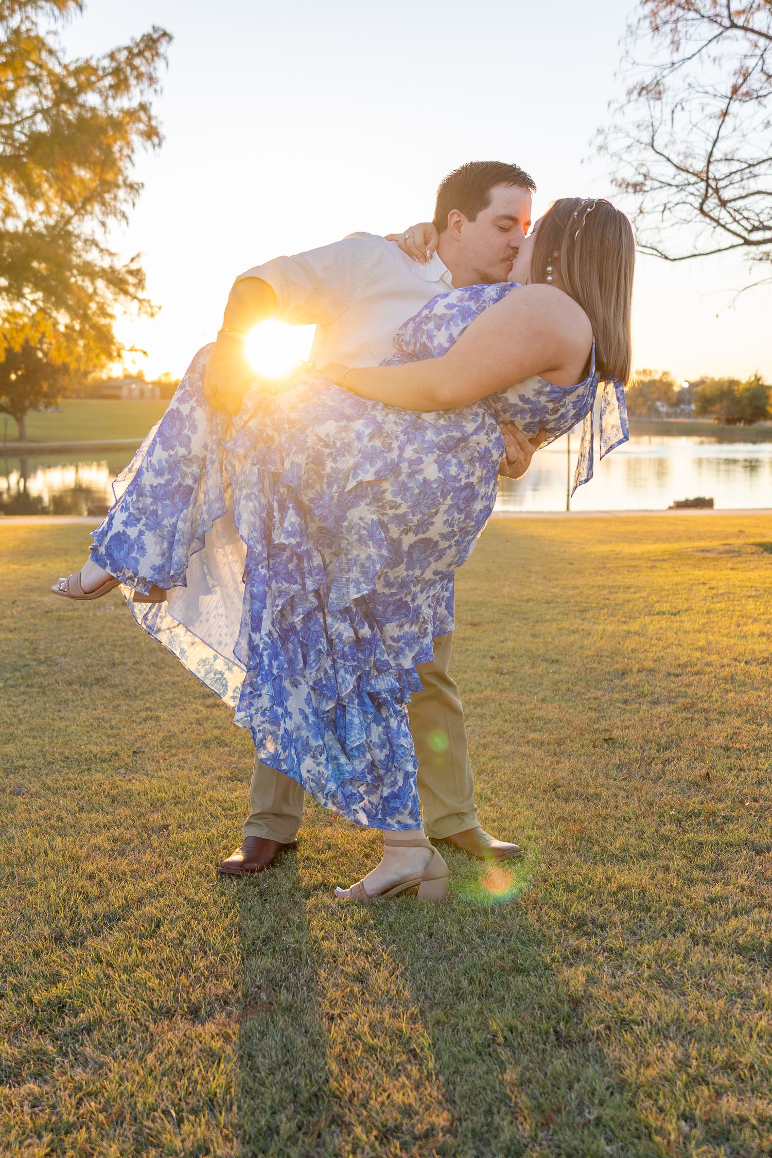 Playful couple dancing in a grassy field during golden hour with sunflare.