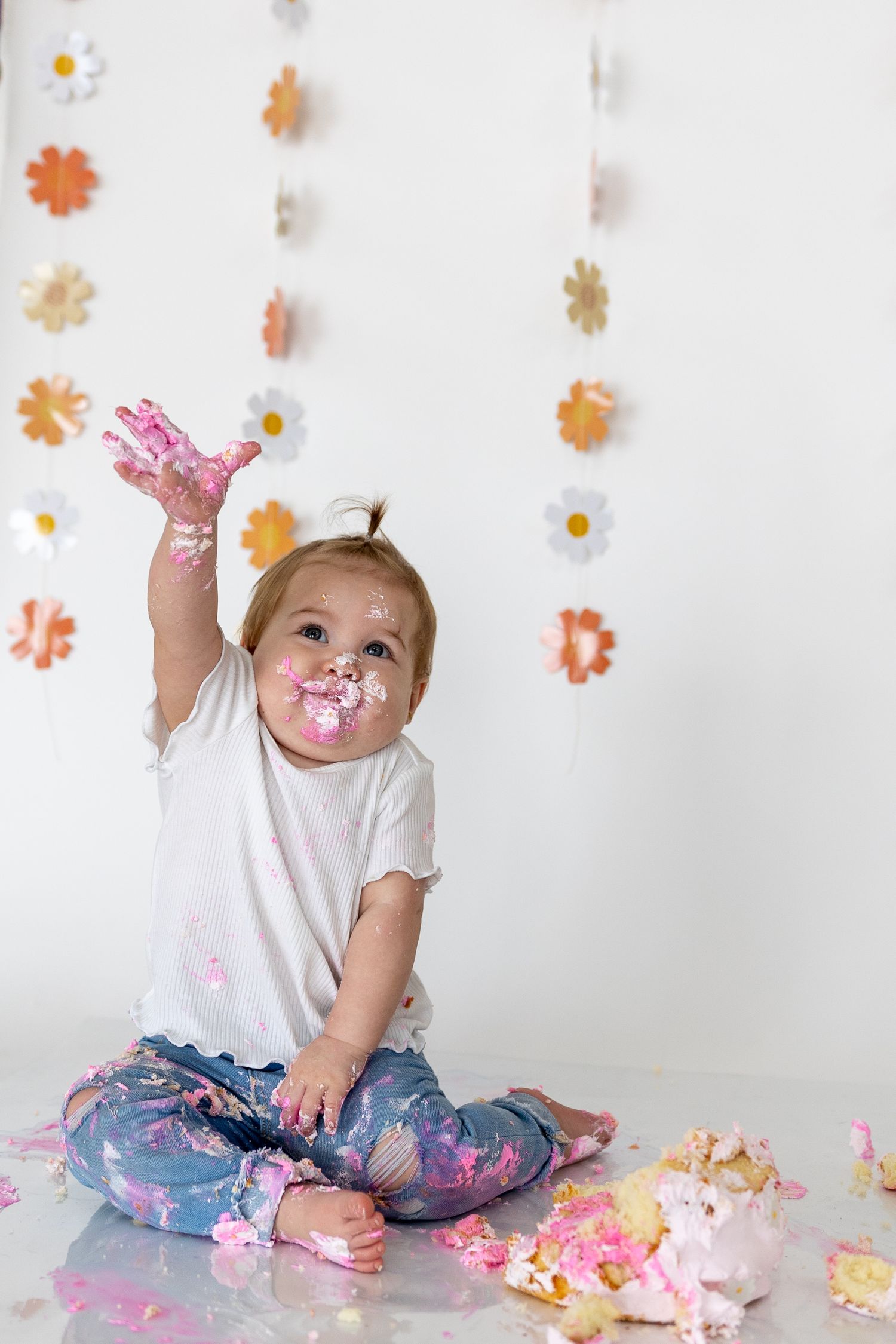 Cake smash photo session with pink and orange flower decorations on white background.