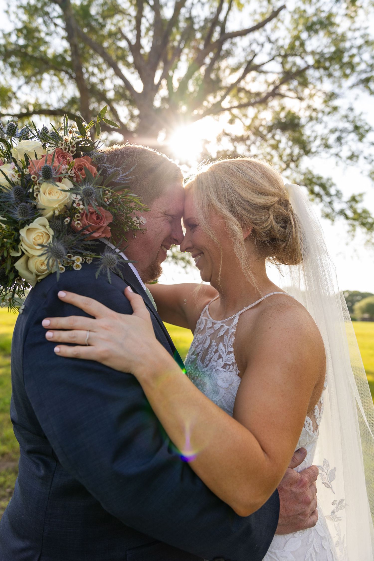 Romantic sunset wedding photo showing couple embracing outdoors with soft golden light filtering through trees.