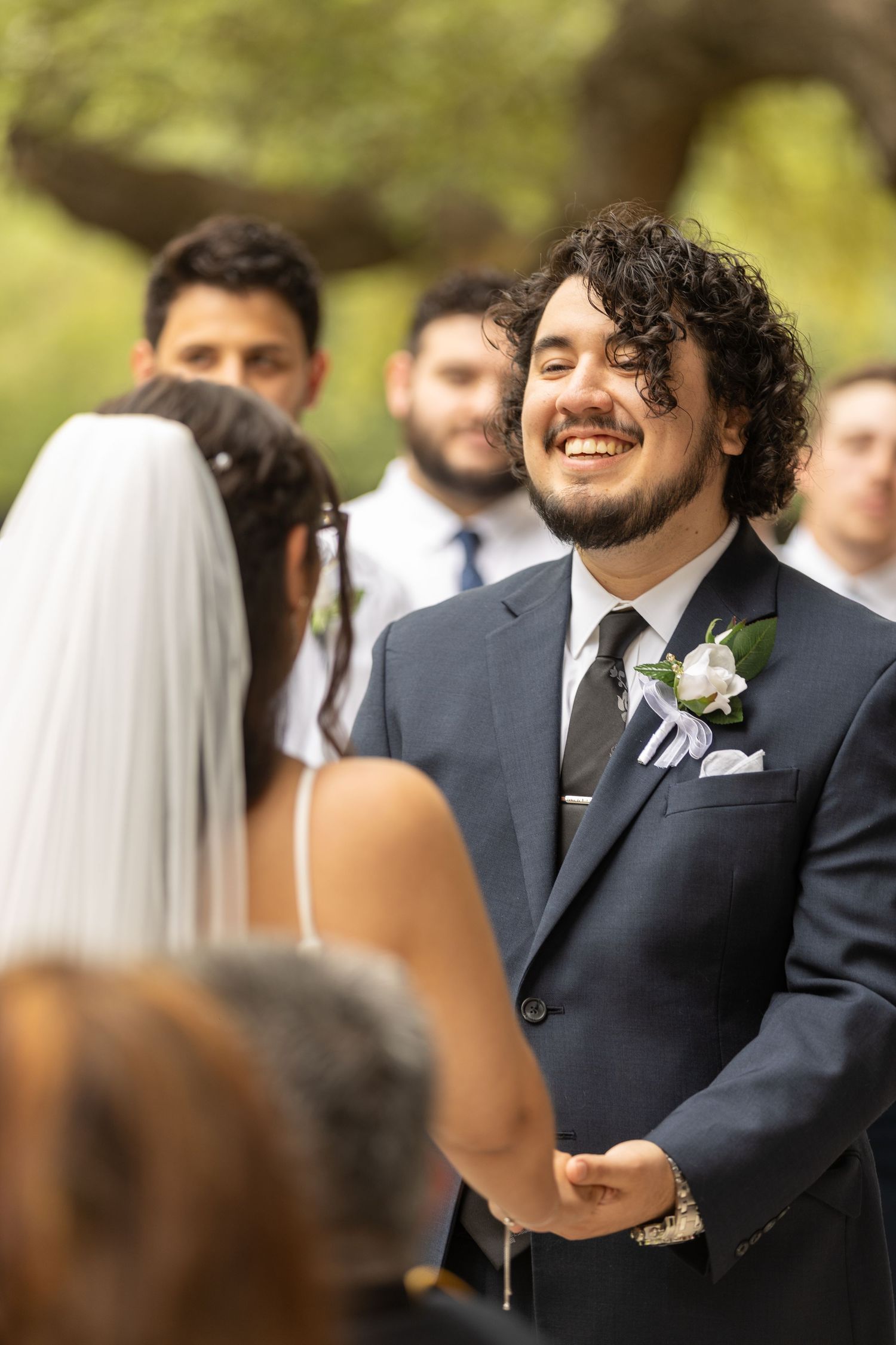 Wedding guests and groomsmen in navy suits share joyful moments during an outdoor ceremony.
