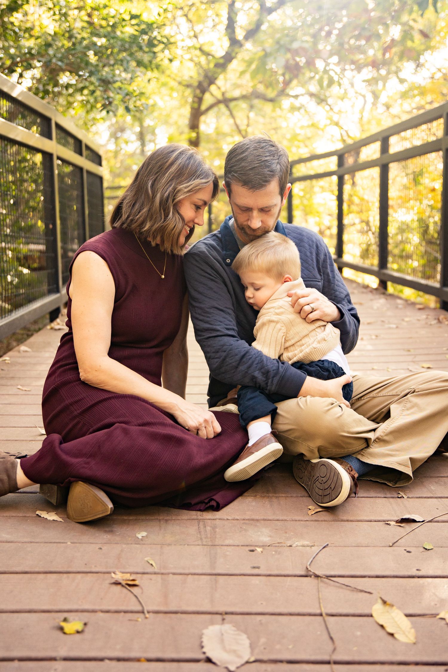 Family sits together on wooden bridge deck surrounded by autumn foliage.