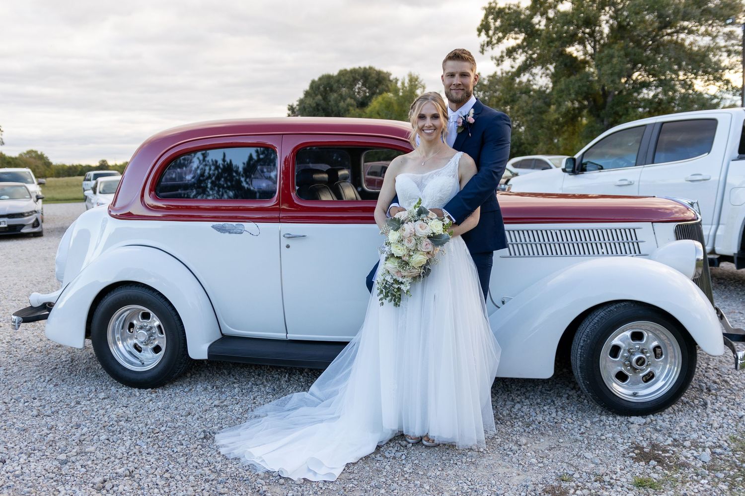 Classic cars serve as elegant props for wedding photos on a bright outdoor day.